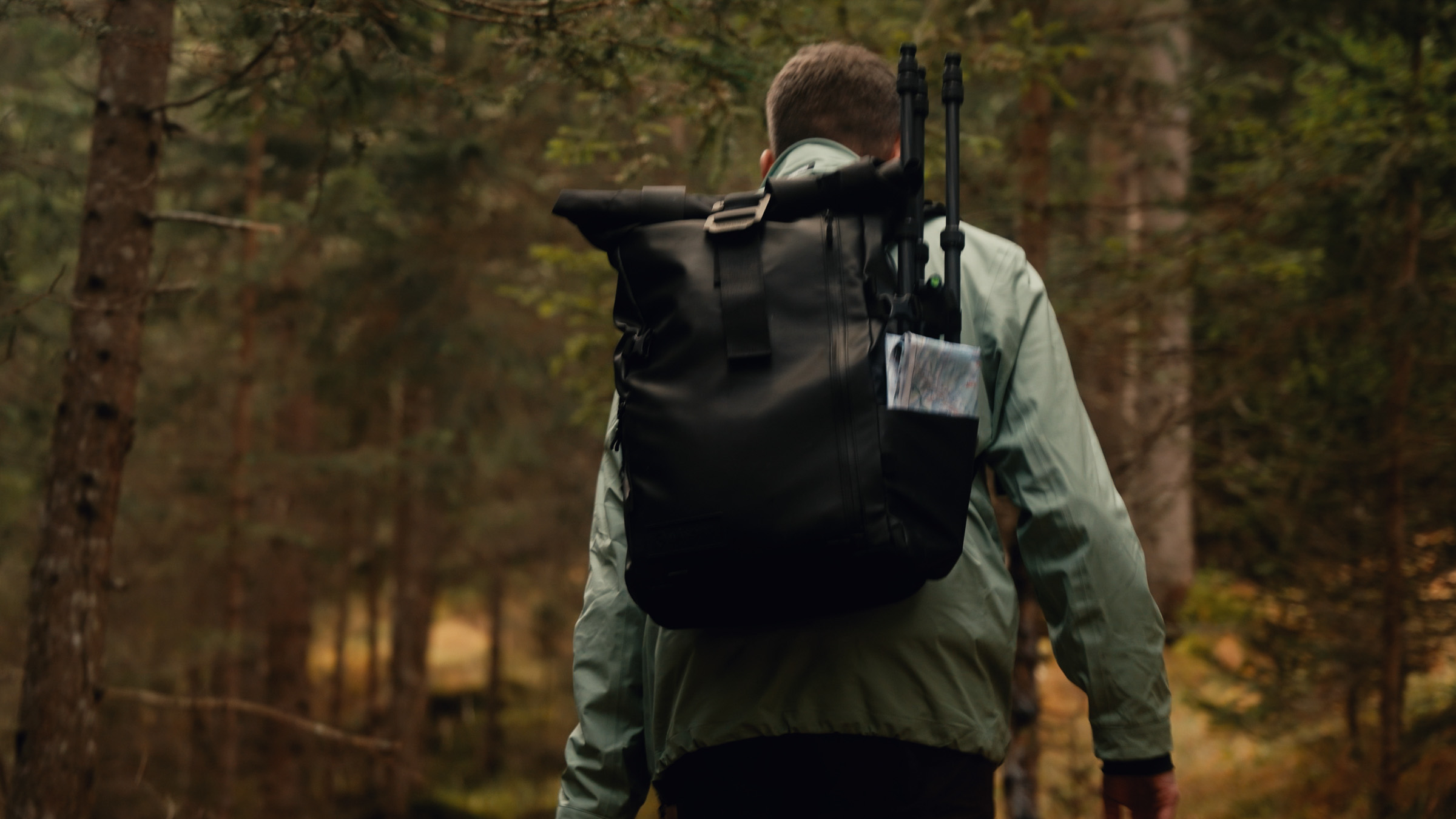 Hiker carrying a black backpack and tripod through the forest