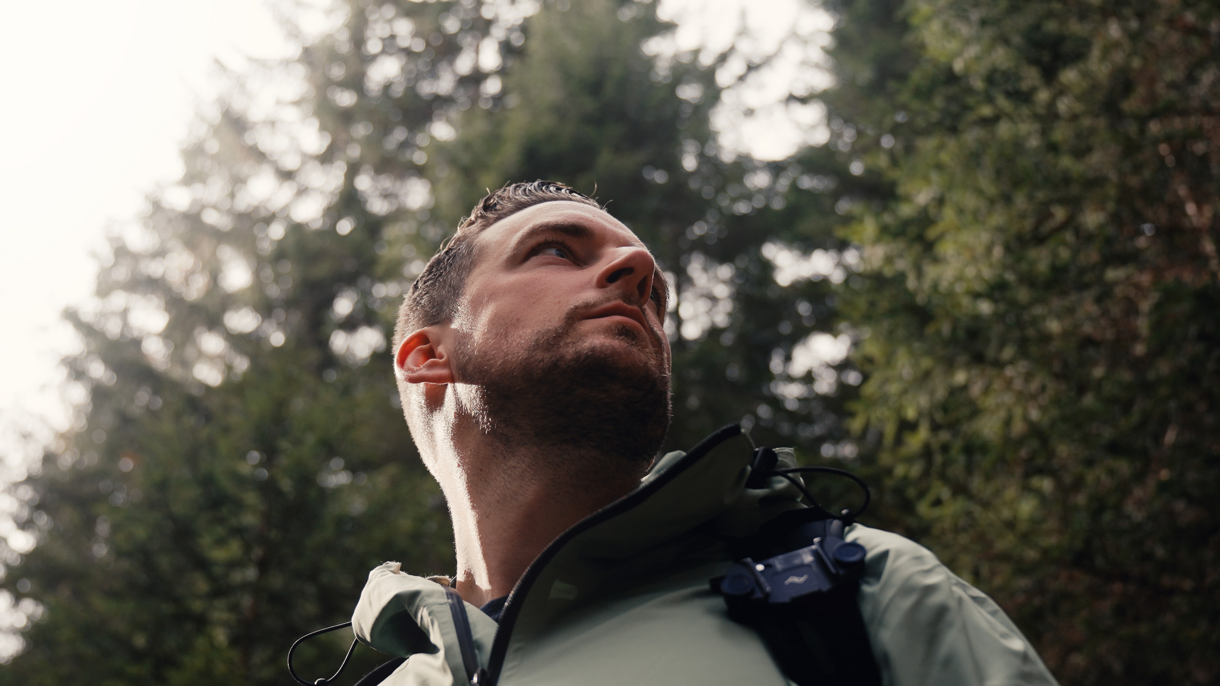 Man in a green Haukland jacket looking up through the trees