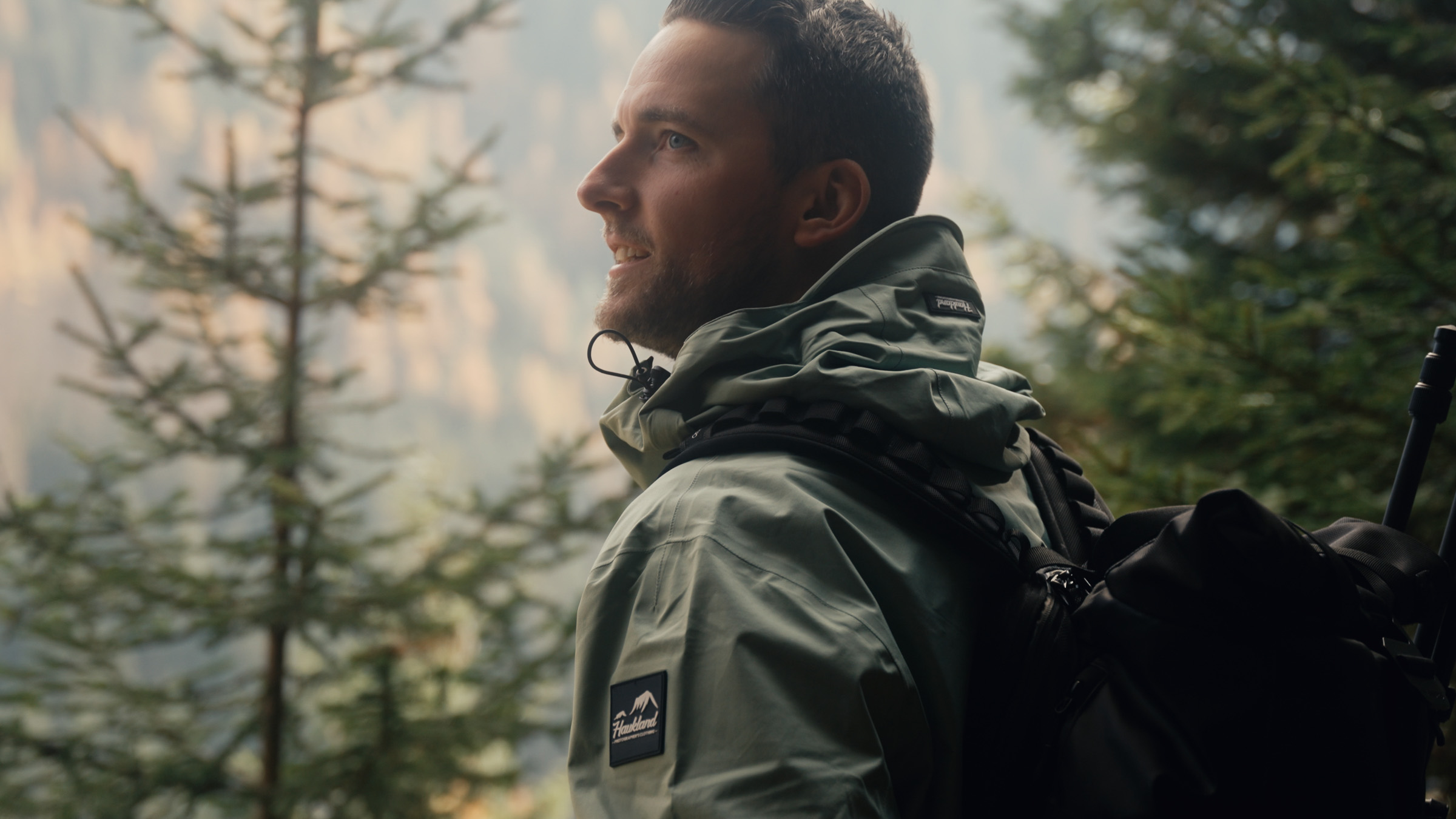 Hiker in a green Haukland jacket standing among mountain trees