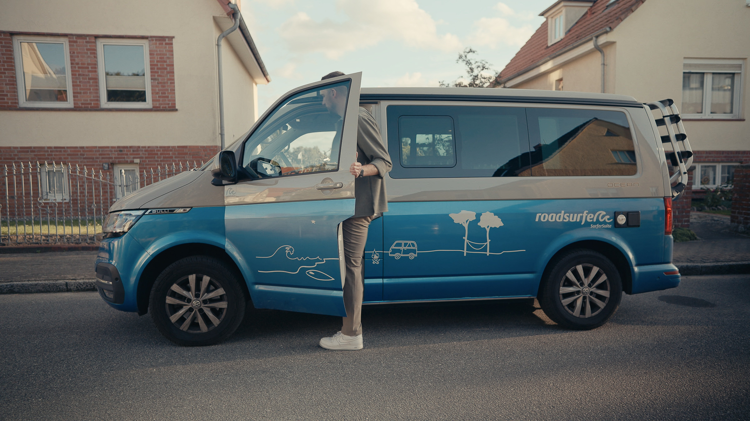 Man opening the driver's door of a blue Roadsurfer camper van