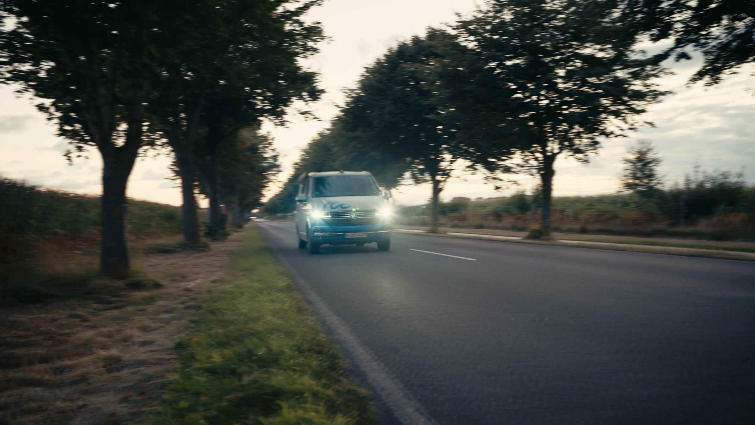 Blue camper van approaching along a tree-lined country road