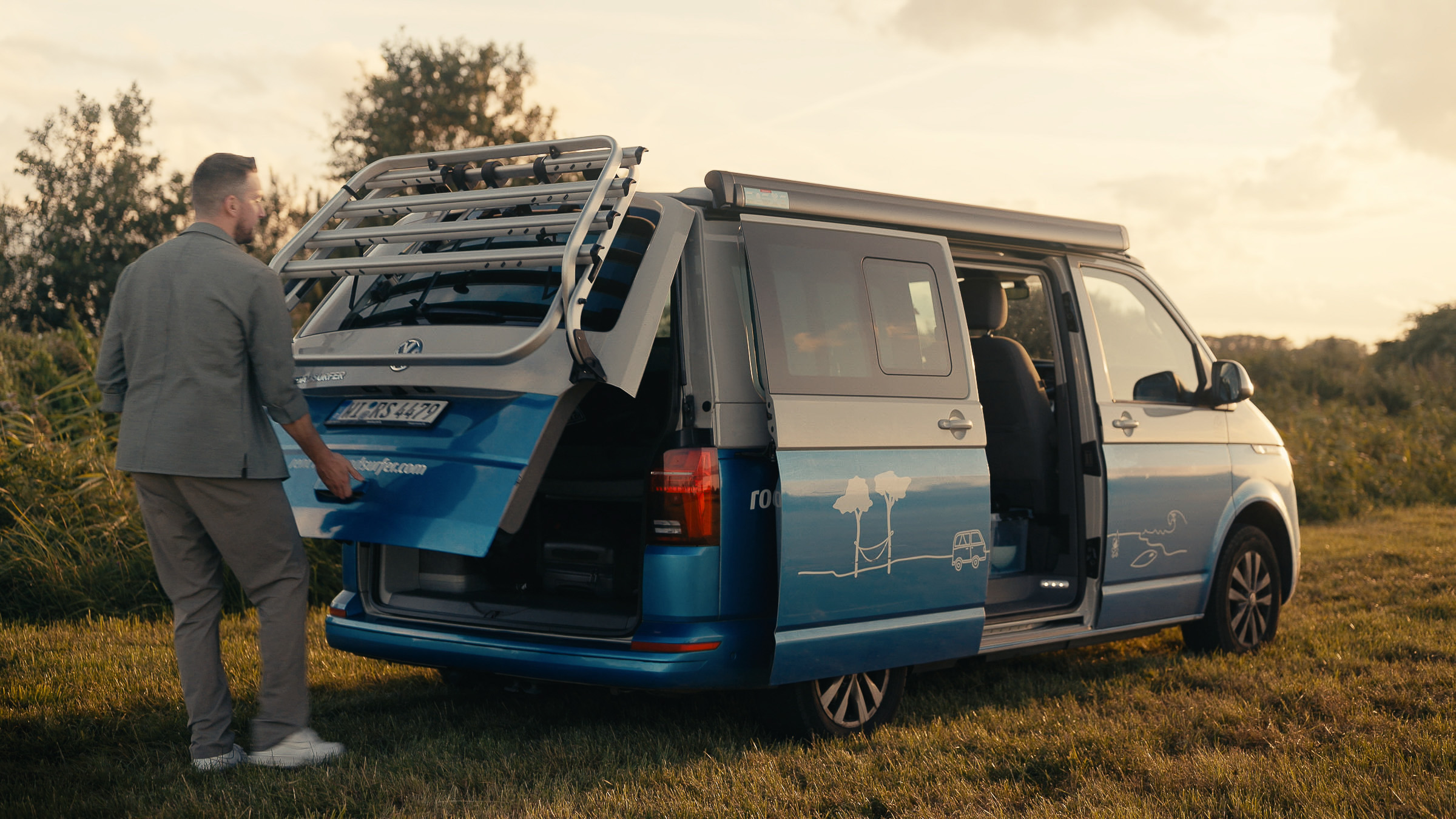 Man opening the rear doors of a blue Roadsurfer camper