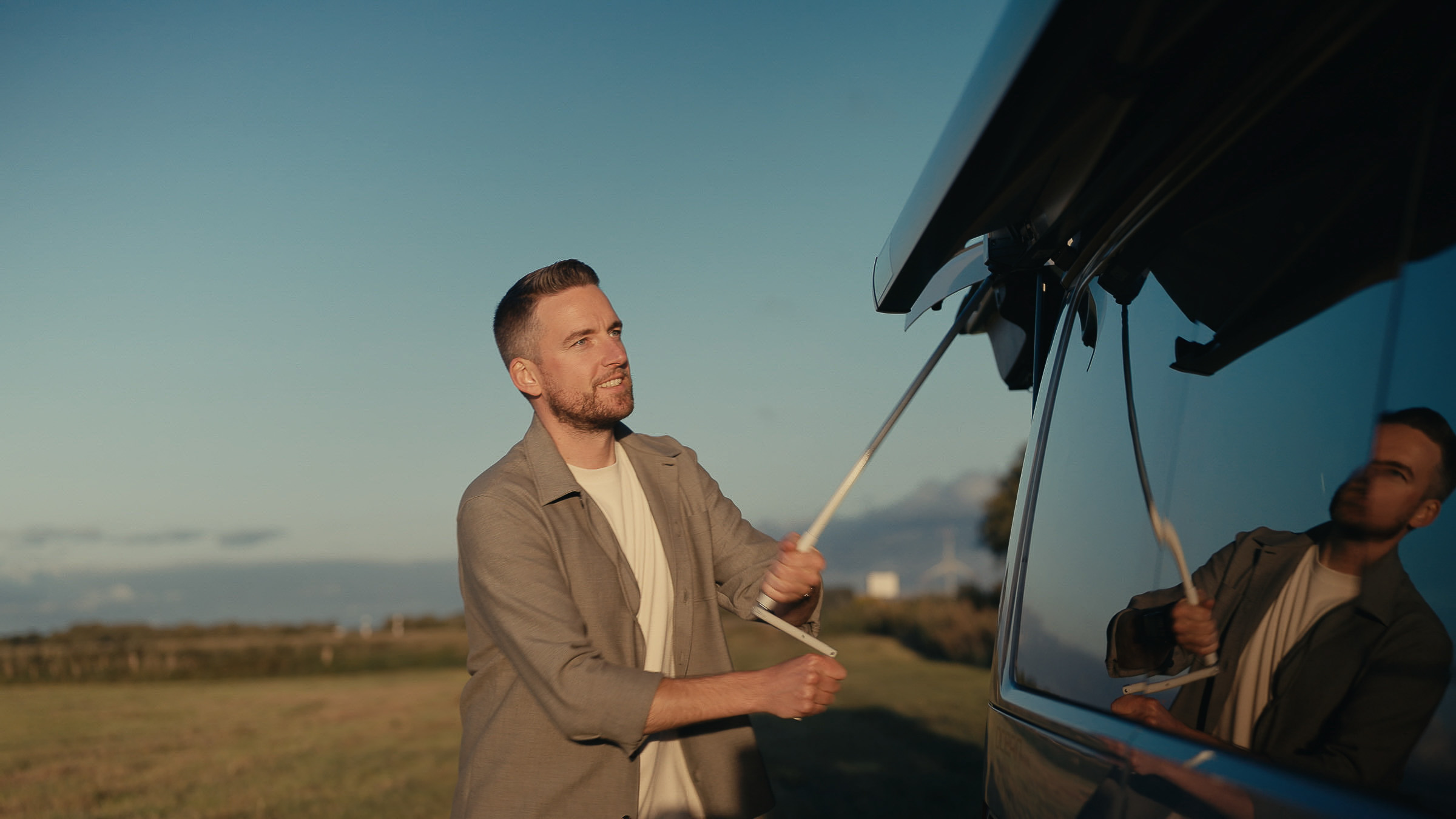 Man extending the awning of a Roadsurfer camper at sunset