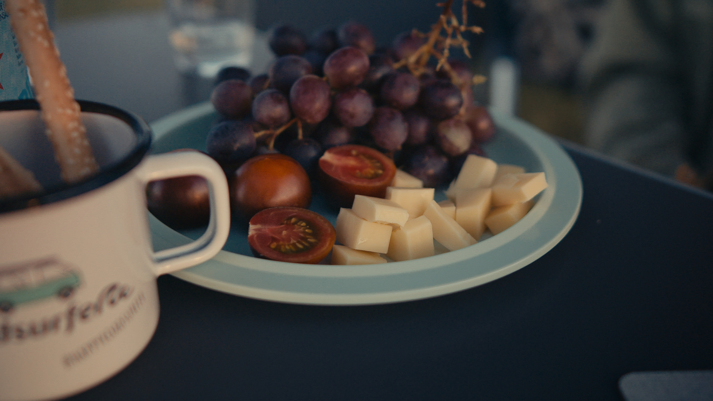 Plate of grapes, cheese and fruit beside a Roadsurfer mug