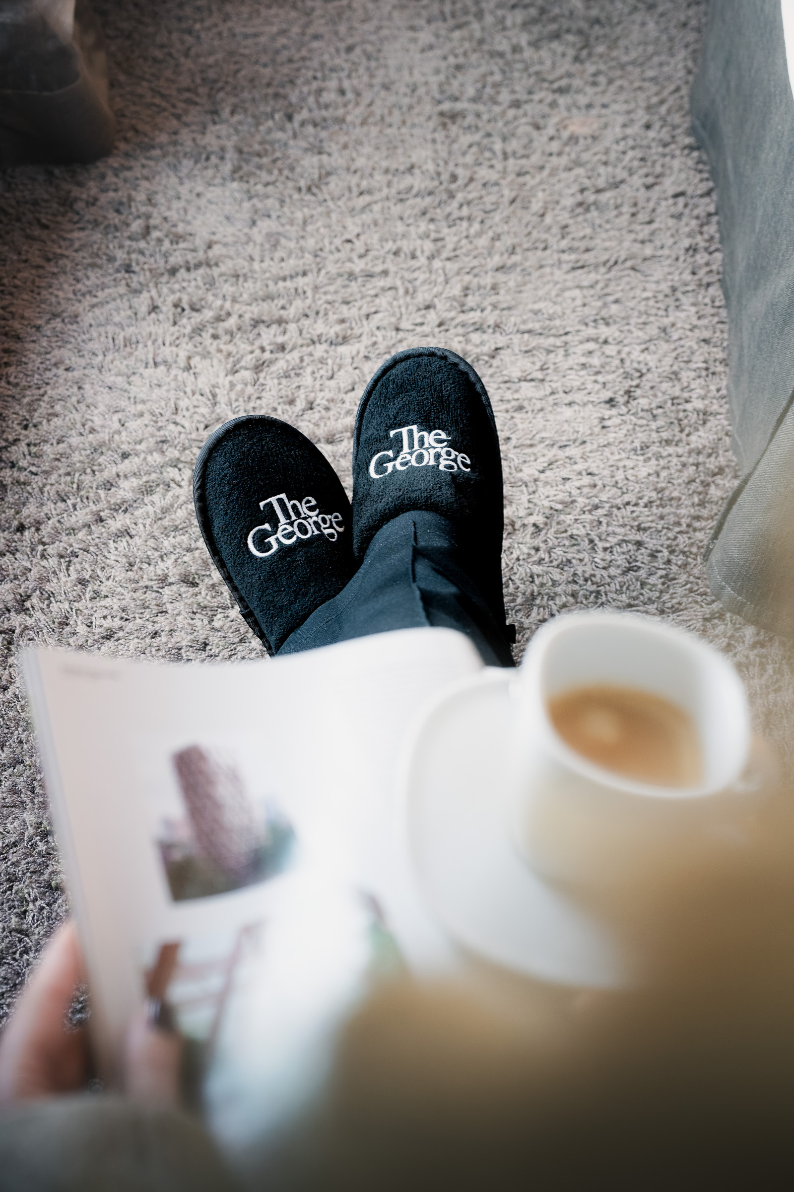 The George slippers, a coffee cup and a magazine on a hotel room bed