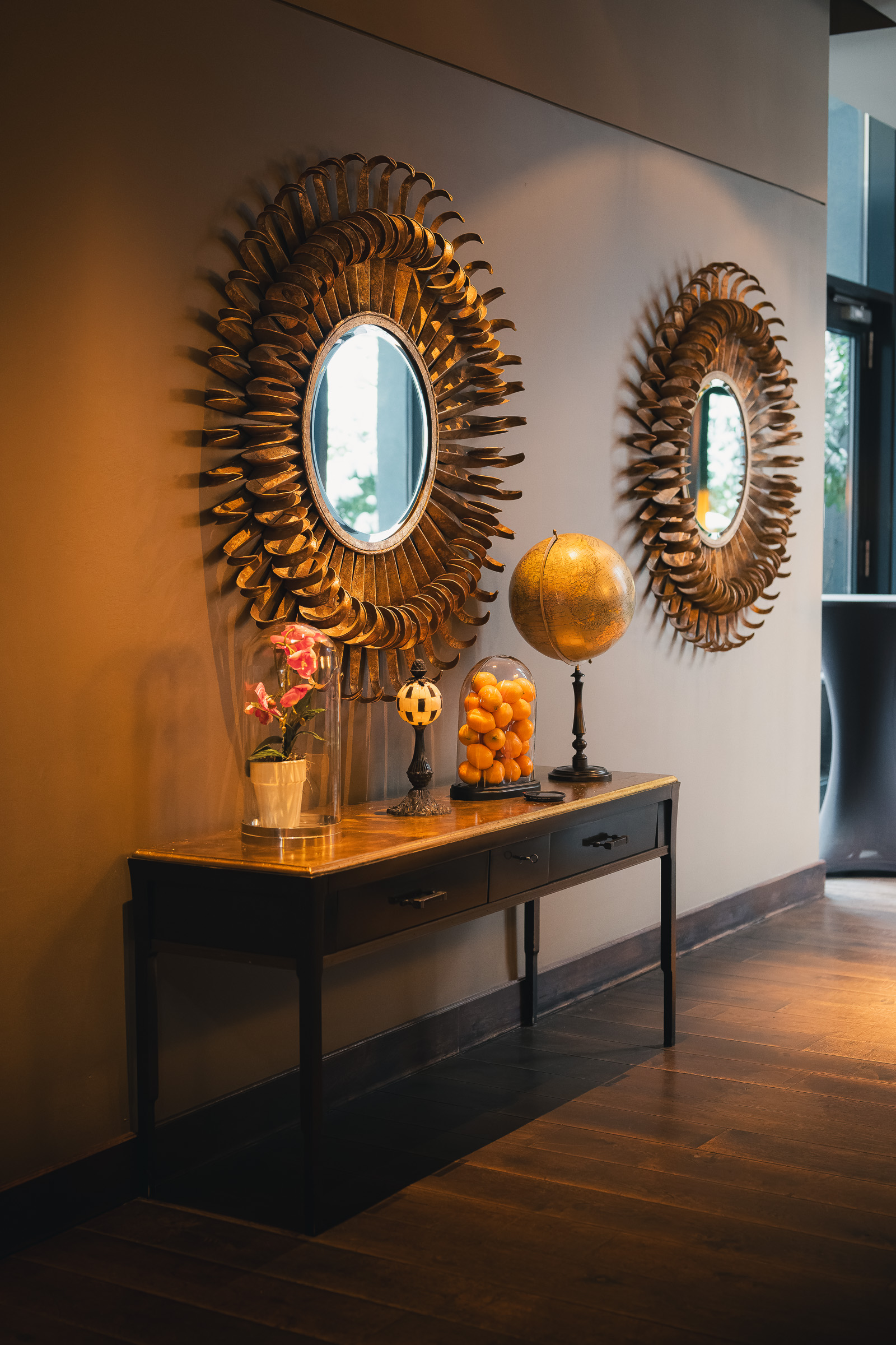 Console table with flowers beneath two sunburst mirrors