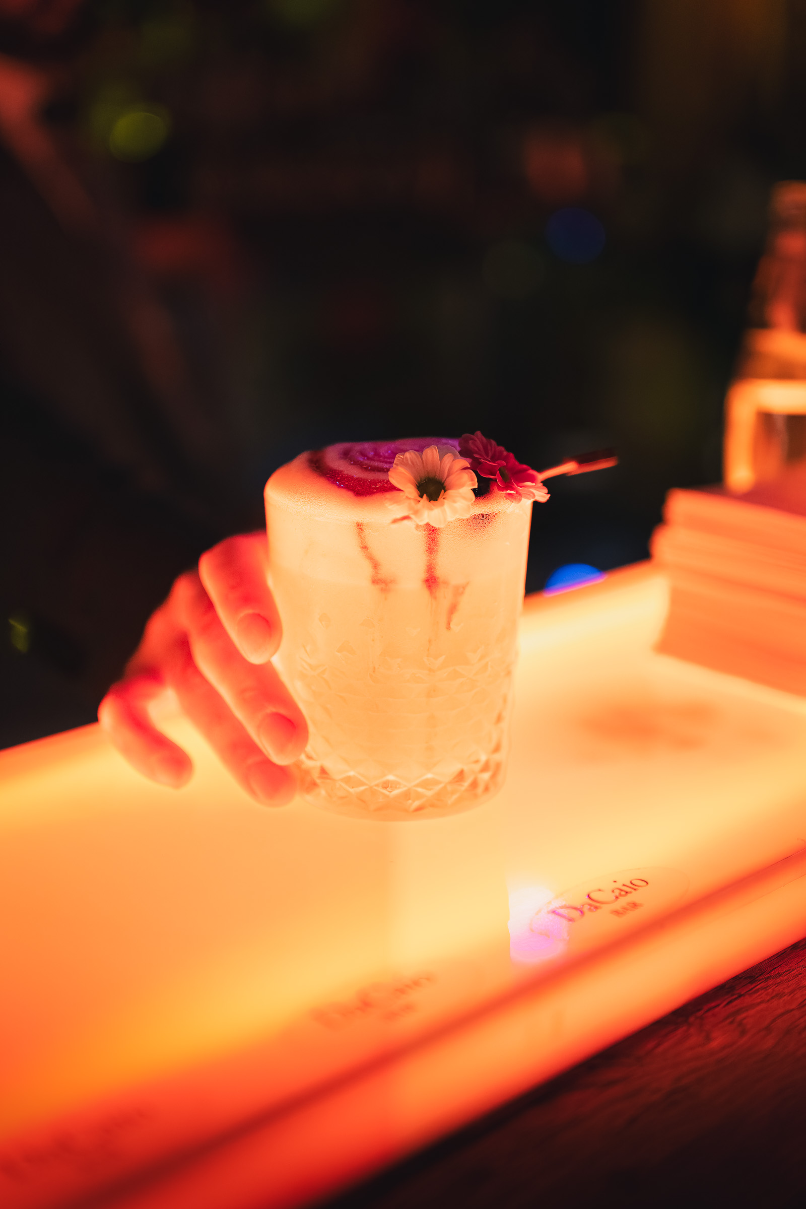 Bartender serving a pale pink cocktail across the illuminated bar