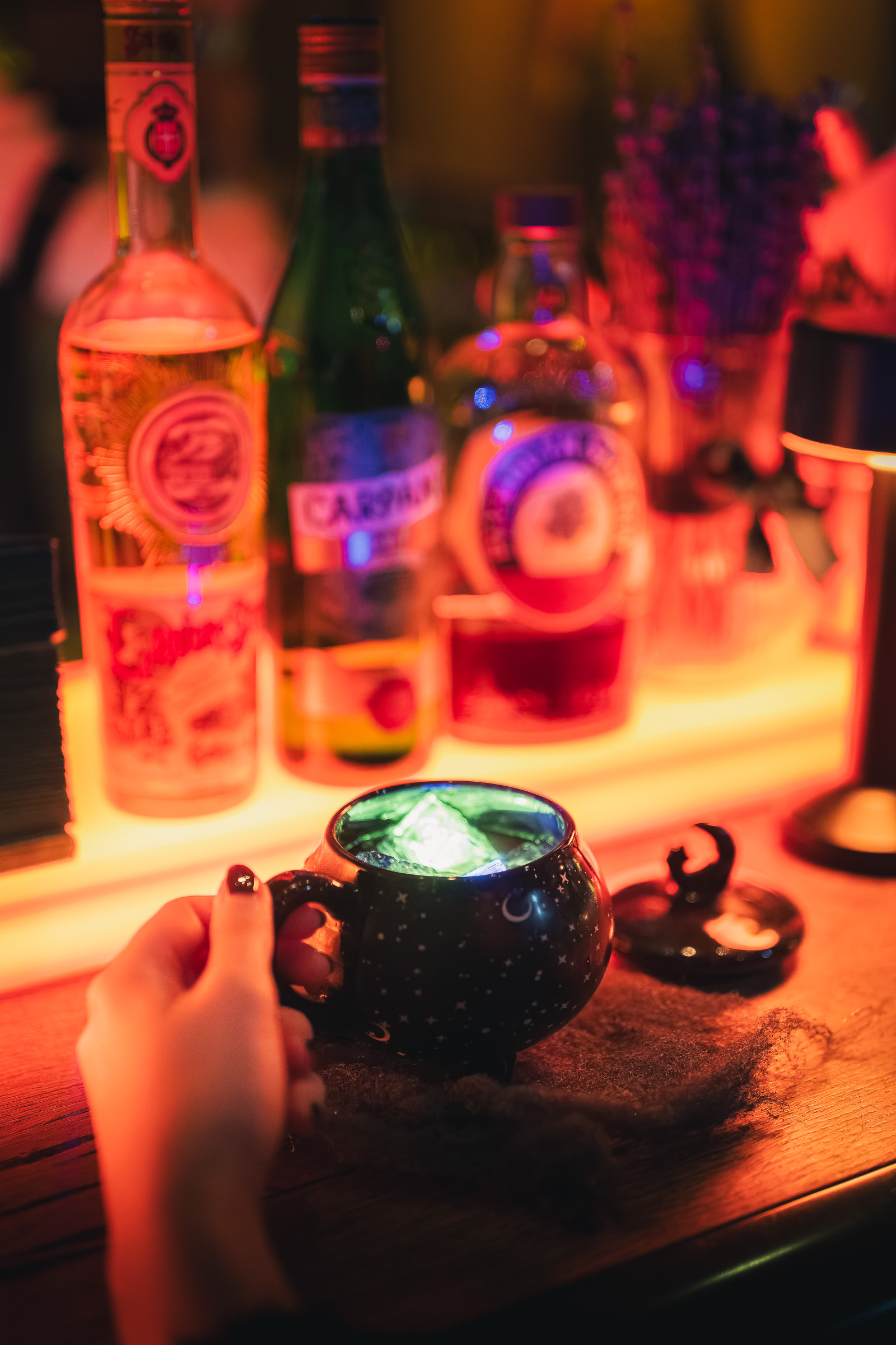 Hand holding a dark blue cocktail in the warm light of the hotel bar