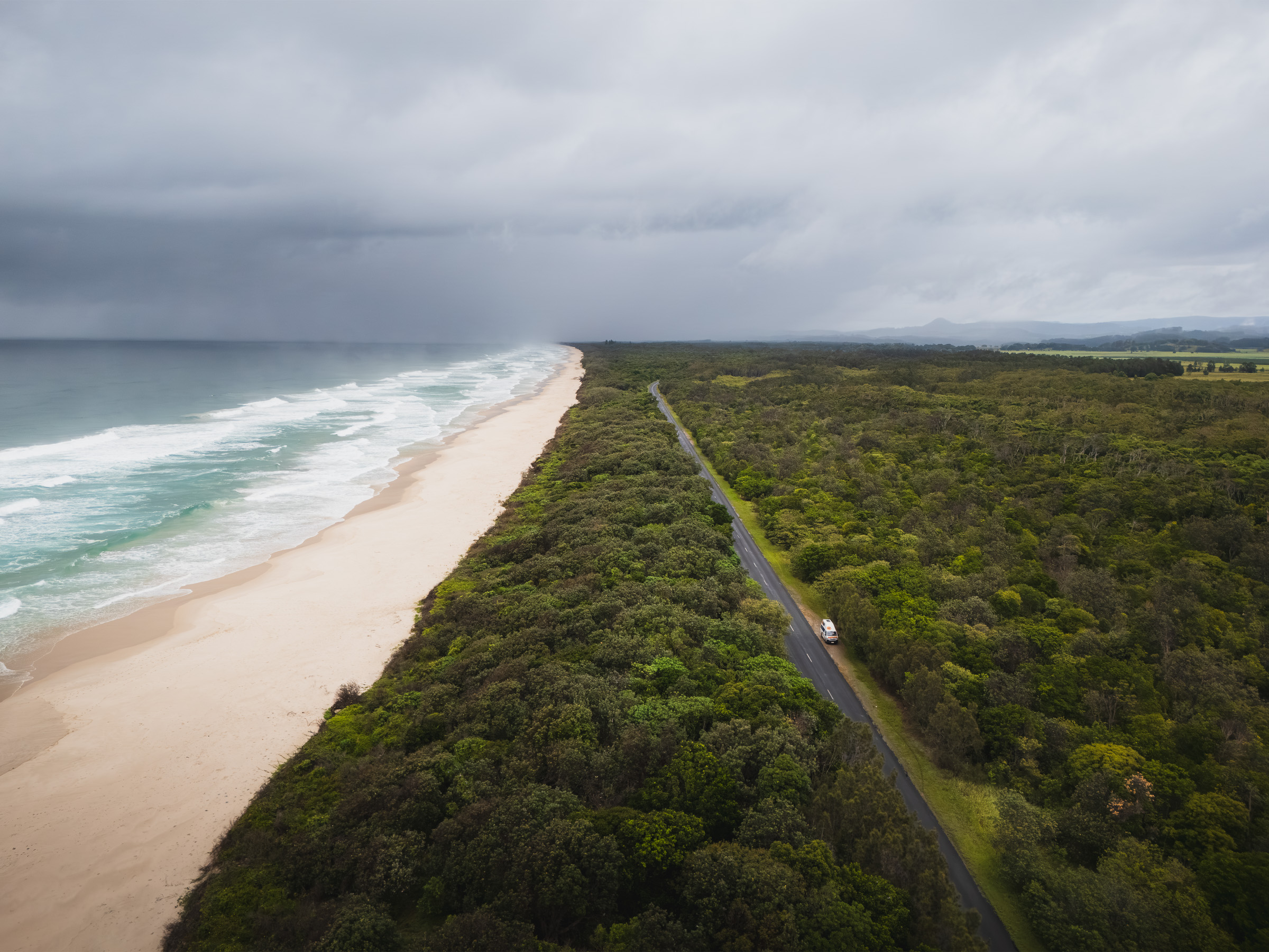 Aerial view of a coastal road beneath storm clouds along an empty beach