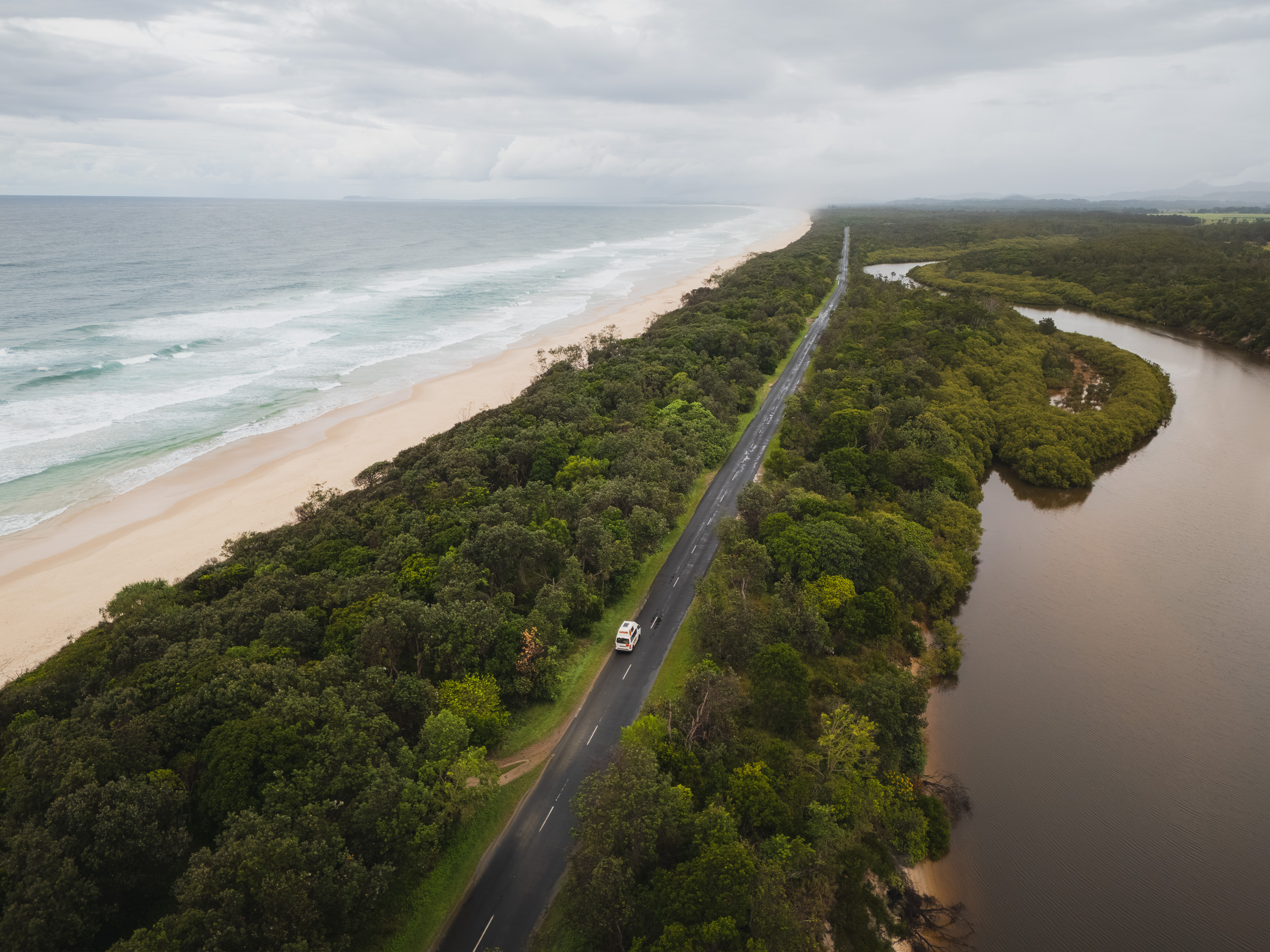 Camper driving a narrow coastal road between the beach and a river