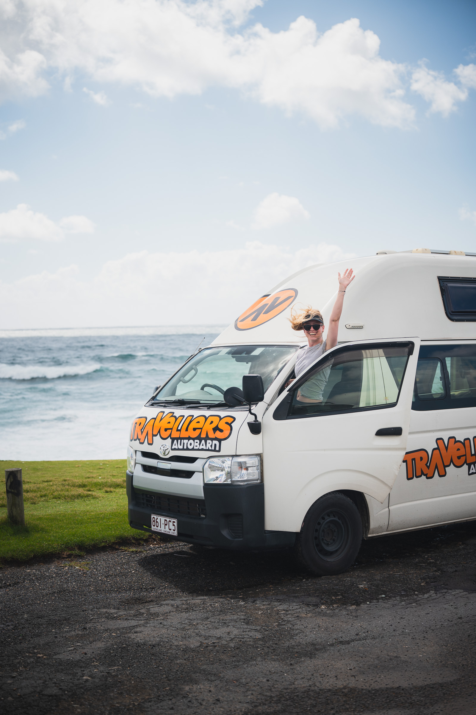 Woman leaning from a Travellers Autobarn camper parked by the ocean