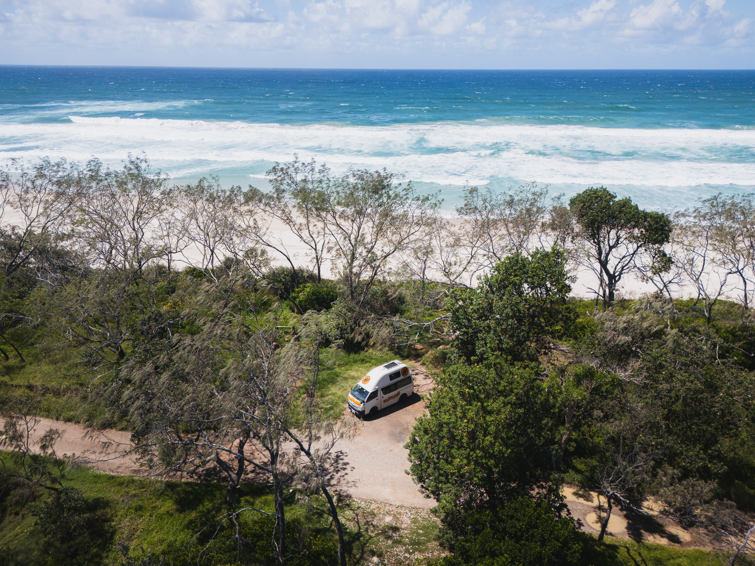 Aerial view of a camper on a sandy track beside the Pacific Ocean