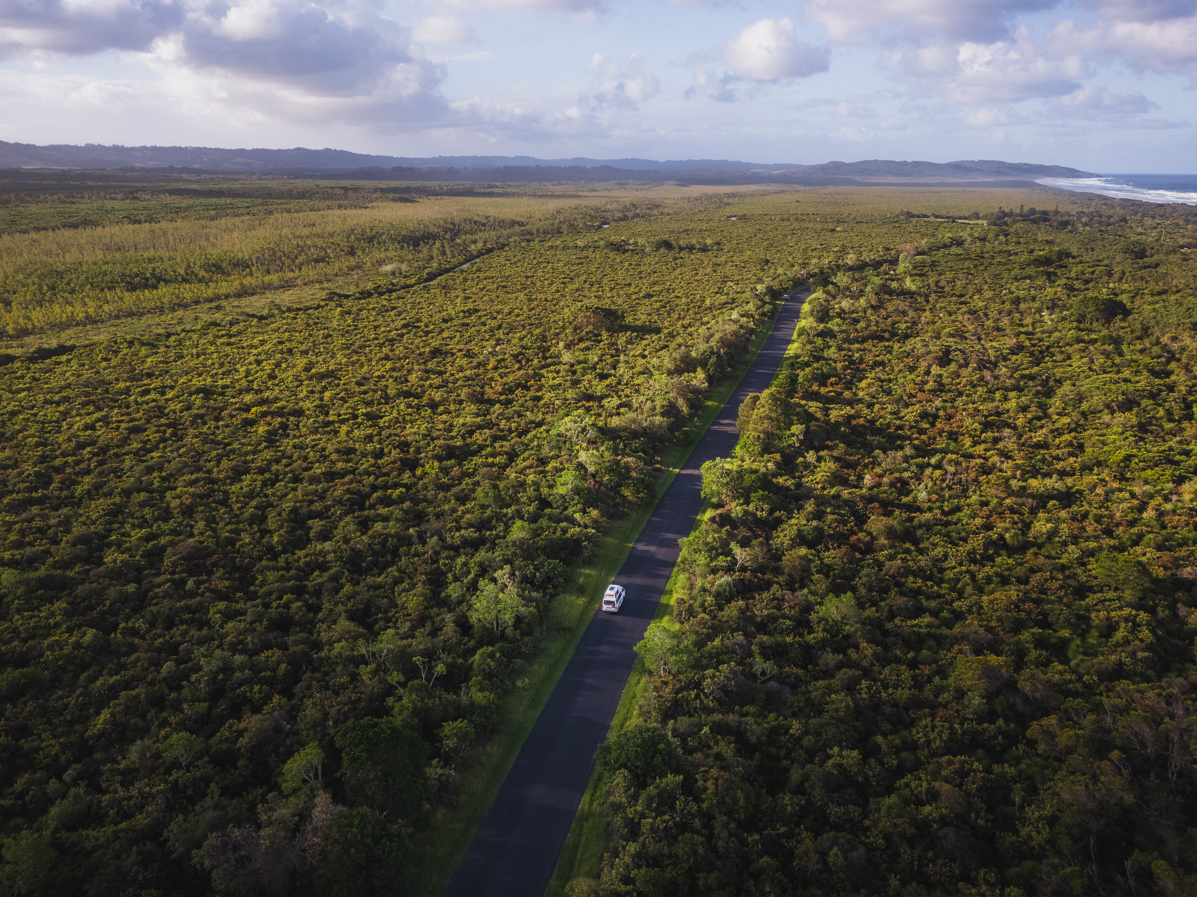 Aerial view of a camper traveling along a straight road through coastal bushland