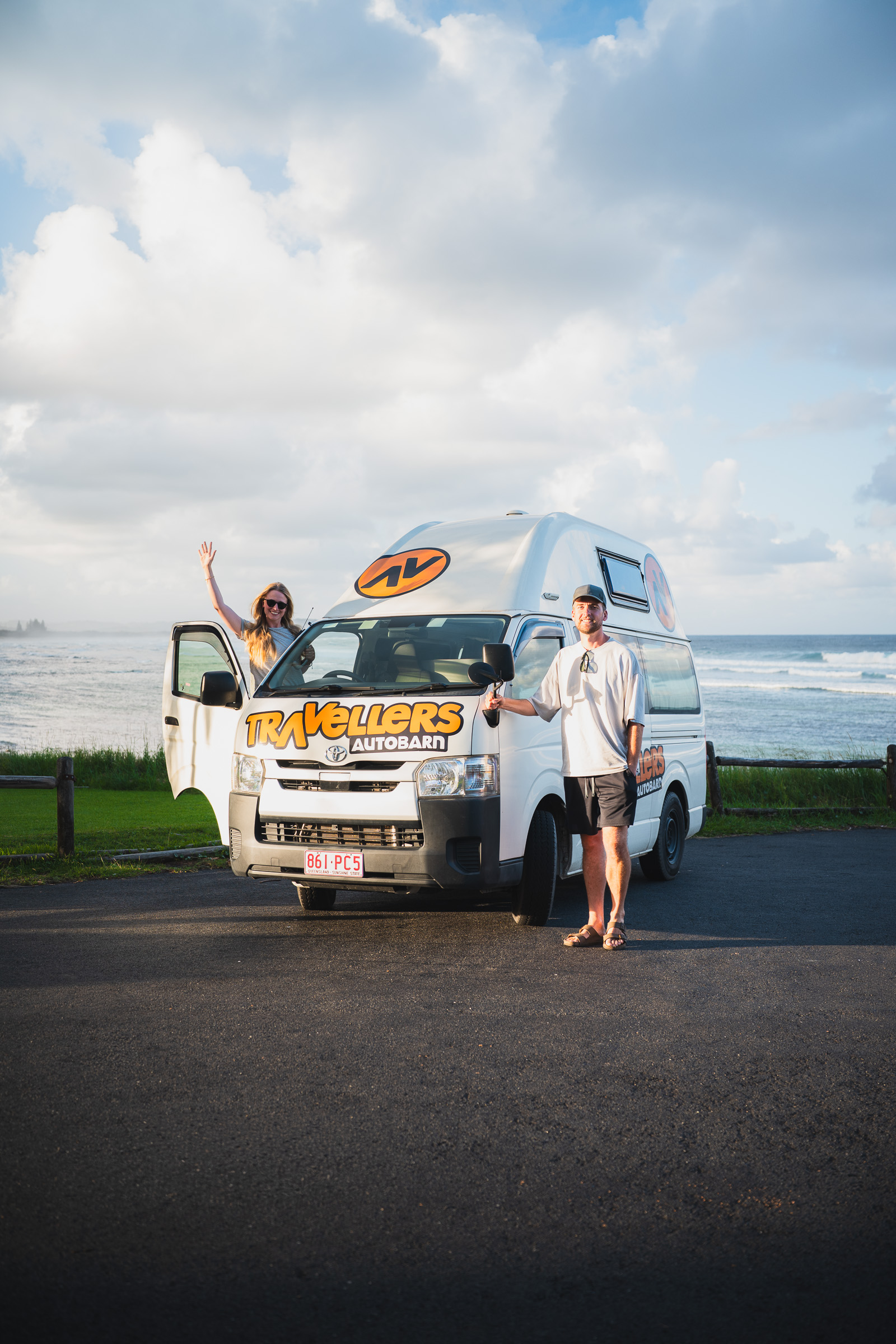 Couple posing with their Travellers Autobarn camper beside the ocean