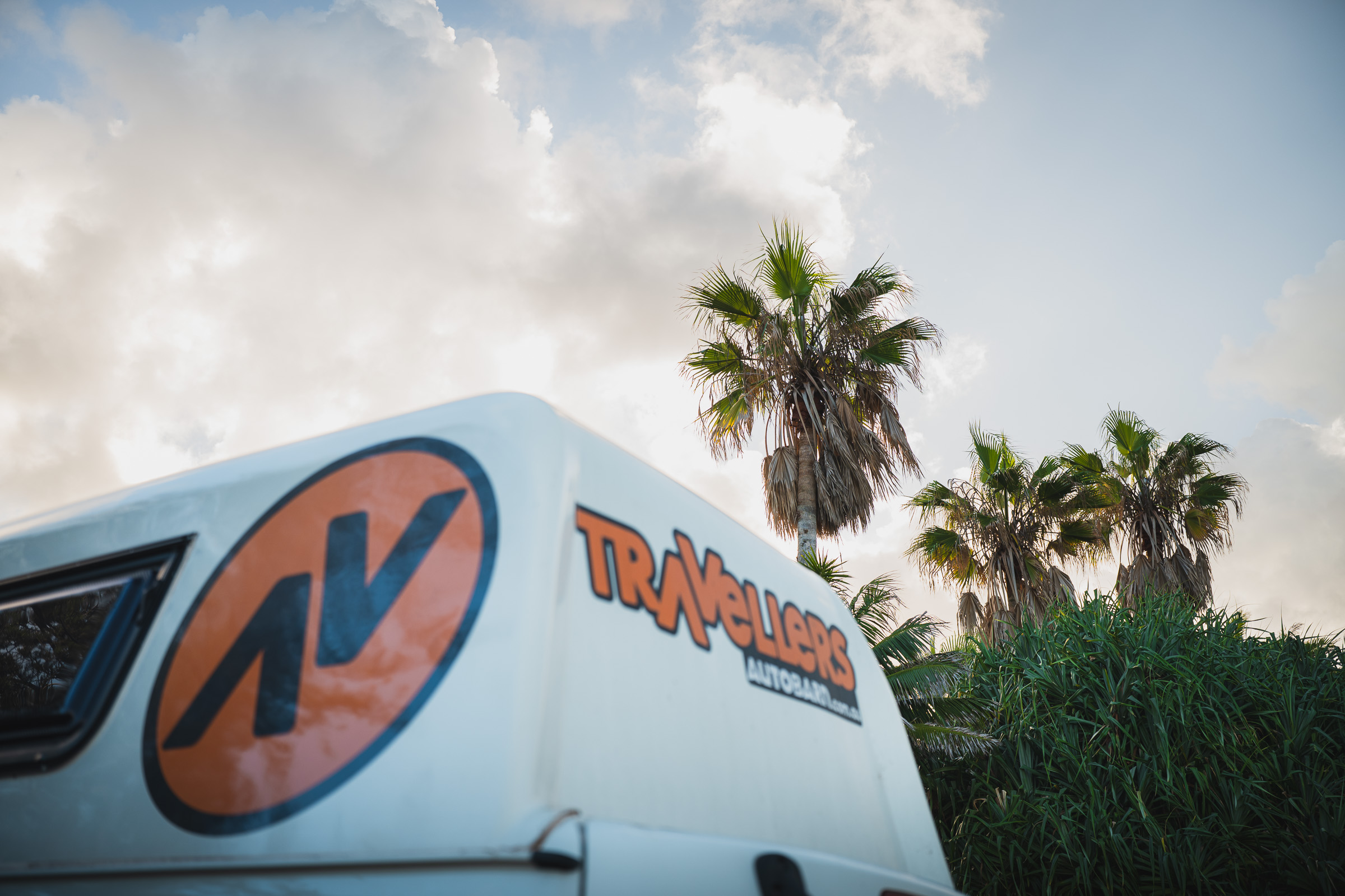 Close-up of the Travellers Autobarn camper logo beneath palm trees