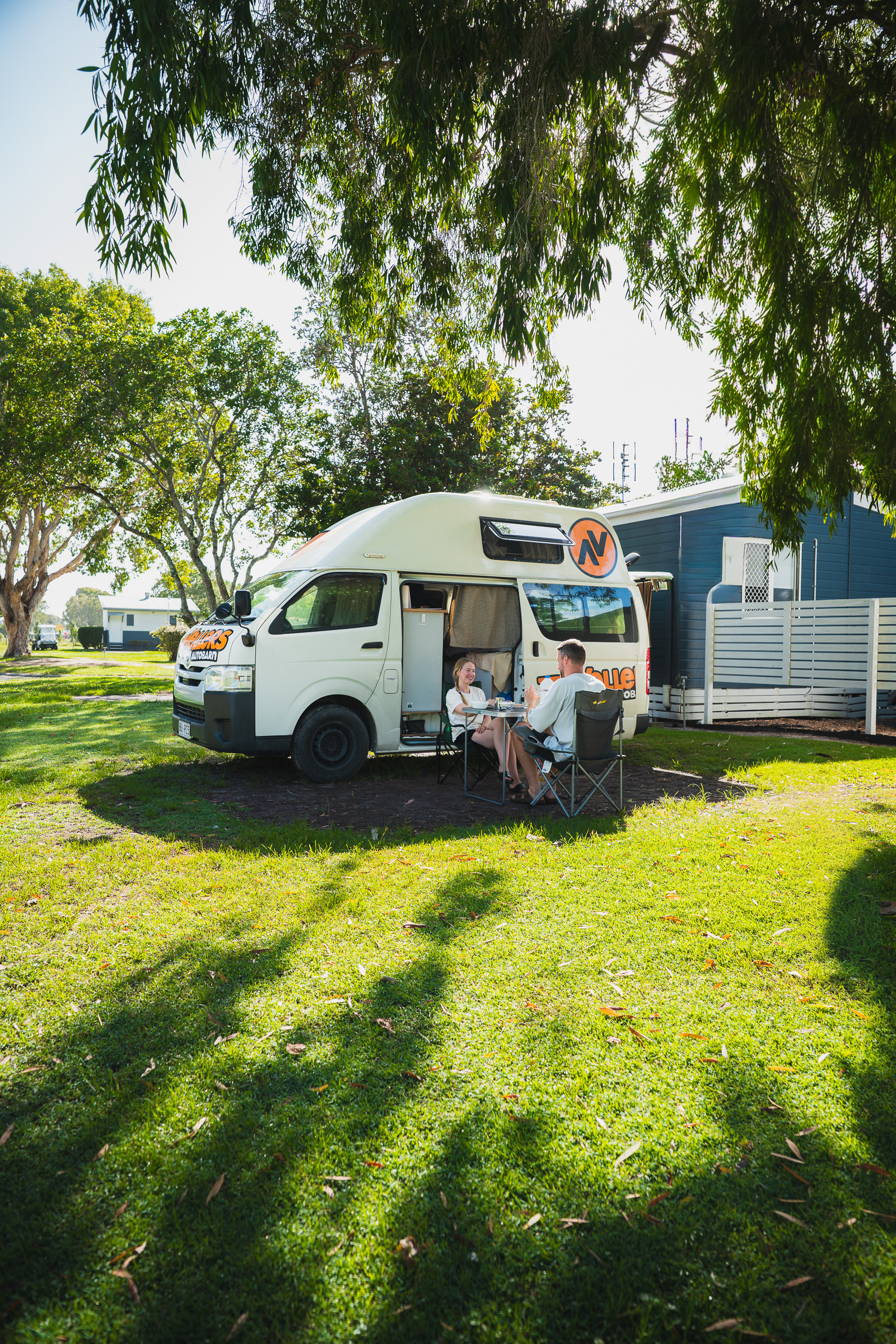 Couple relaxing beside their open camper at a sunny campsite