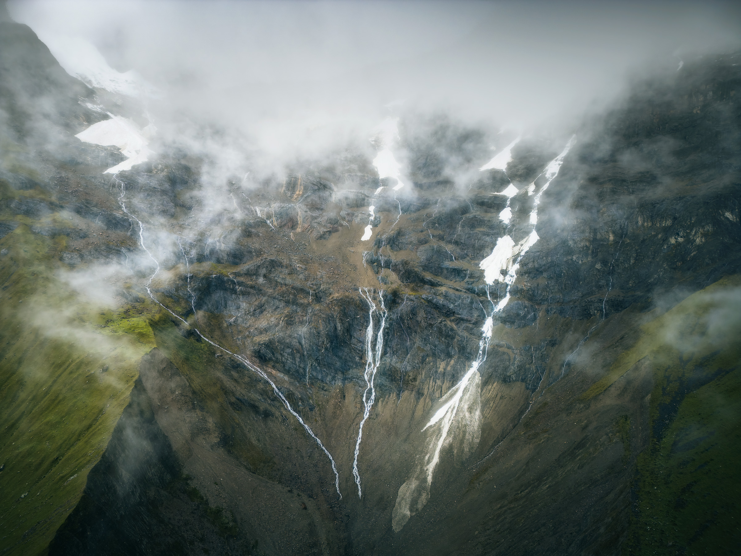 Waterfalls descending a cloud-covered mountain above Humantay Lake