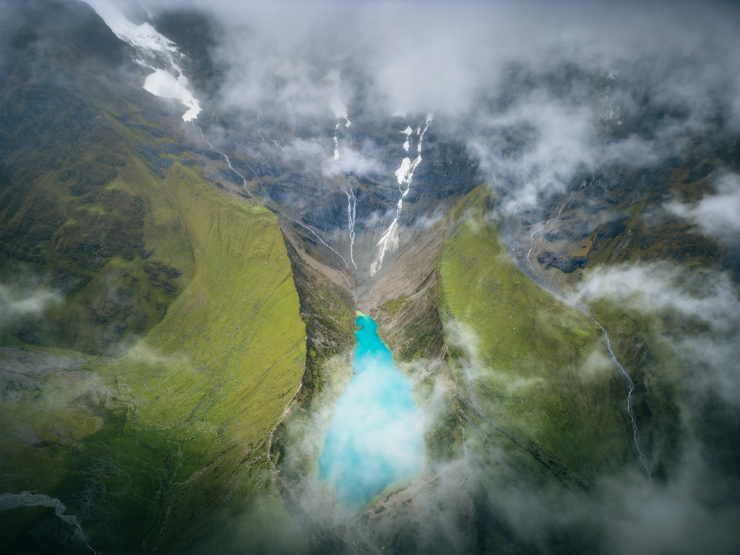 Aerial view of turquoise Humantay Lake beneath cloud-covered mountains