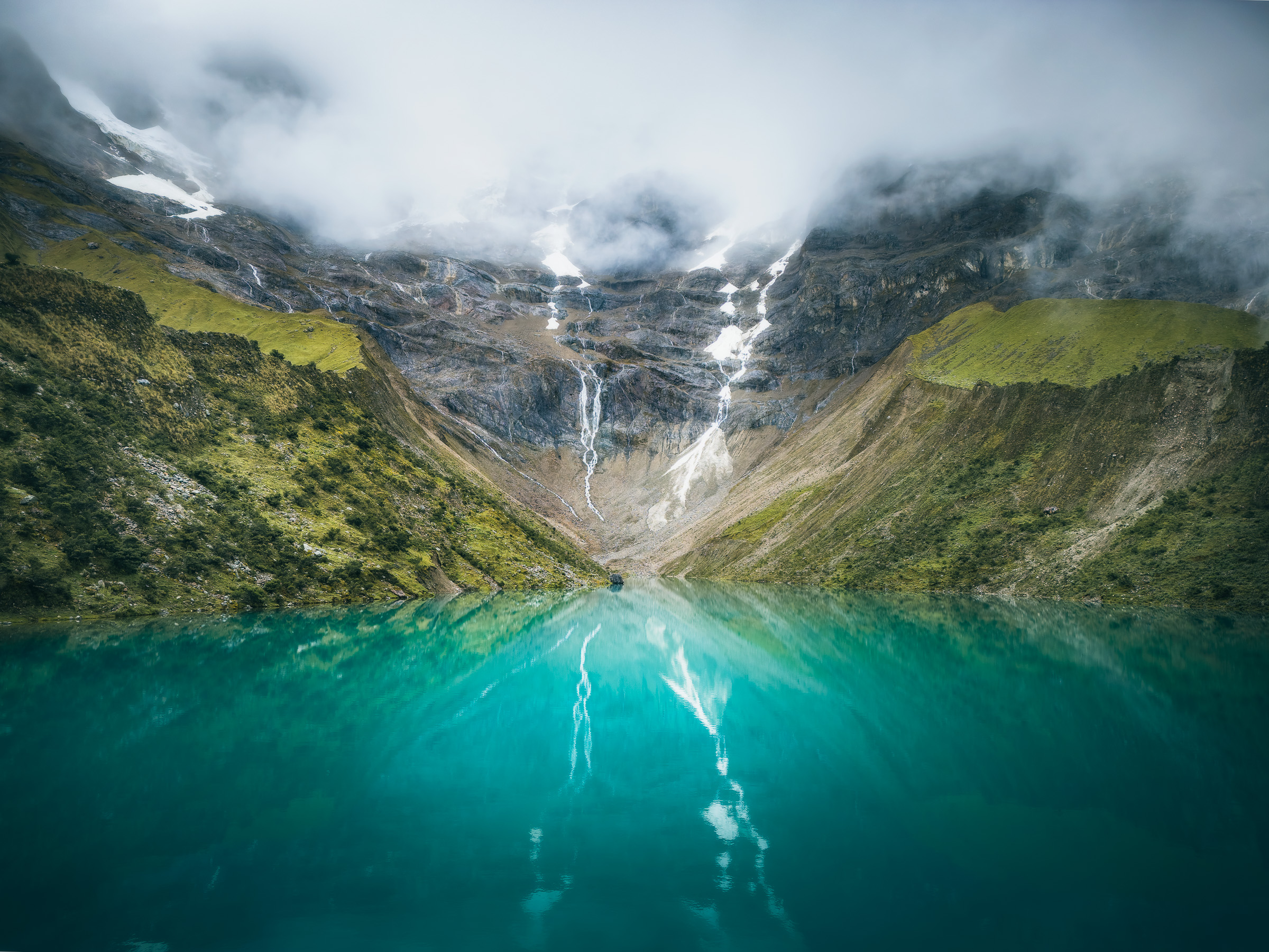 Turquoise Humantay Lake below waterfalls and misty mountain slopes