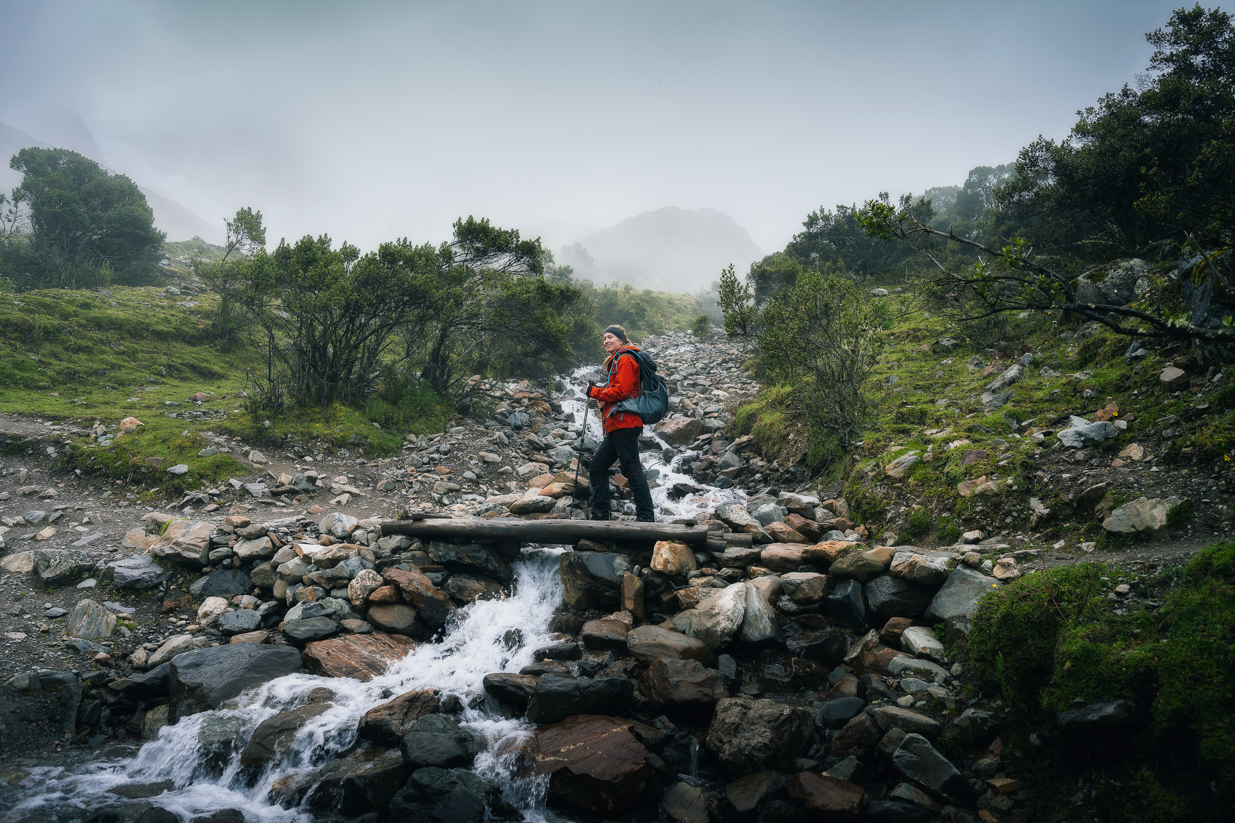 Hiker with an orange jacket crossing a rocky mountain stream