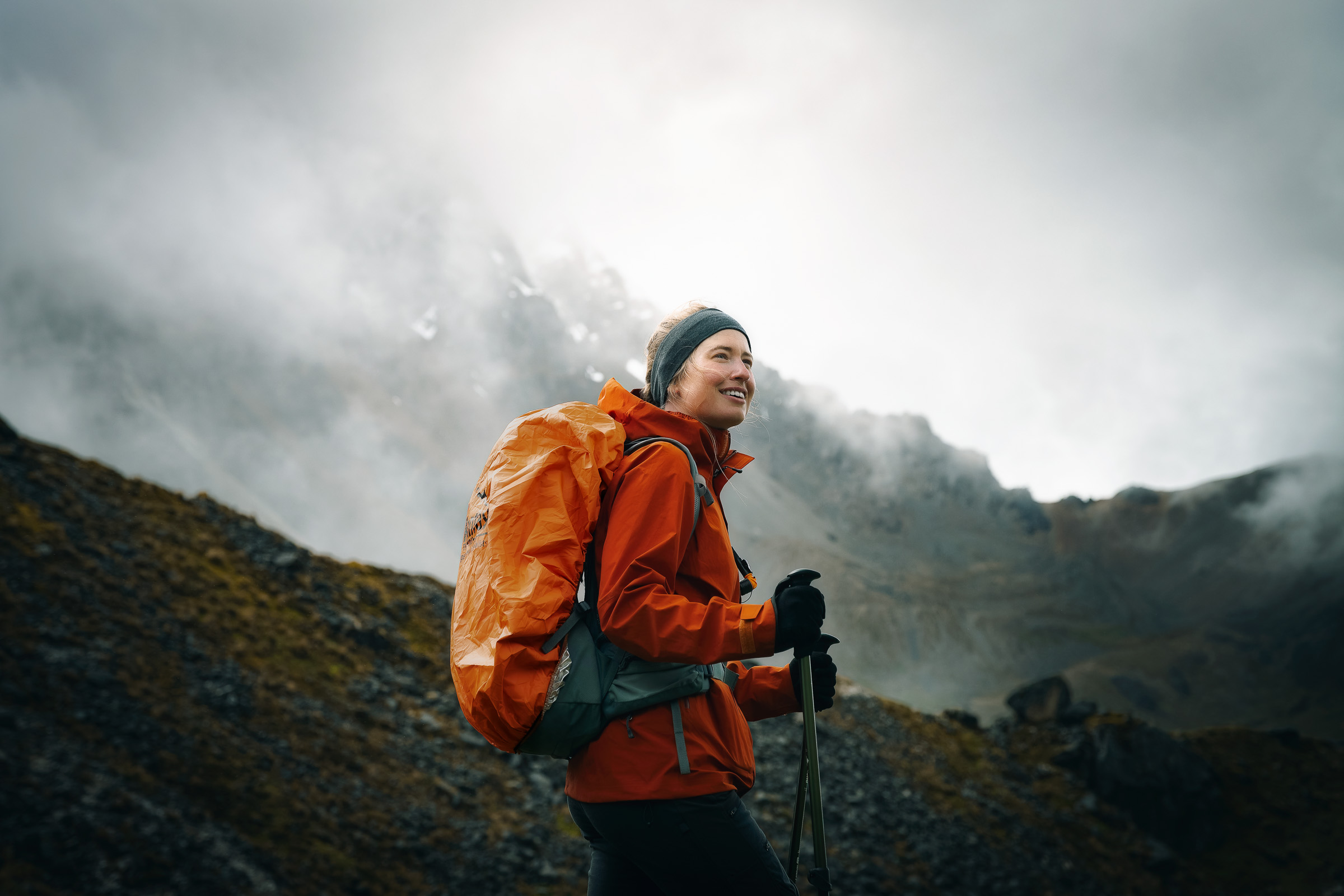 Smiling hiker with trekking poles and an orange backpack in the Andes