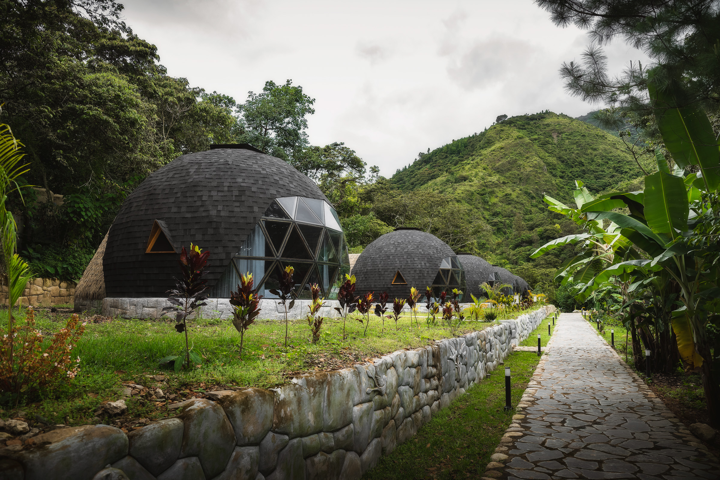 Geodesic mountain lodges beside a stone path in a lush valley