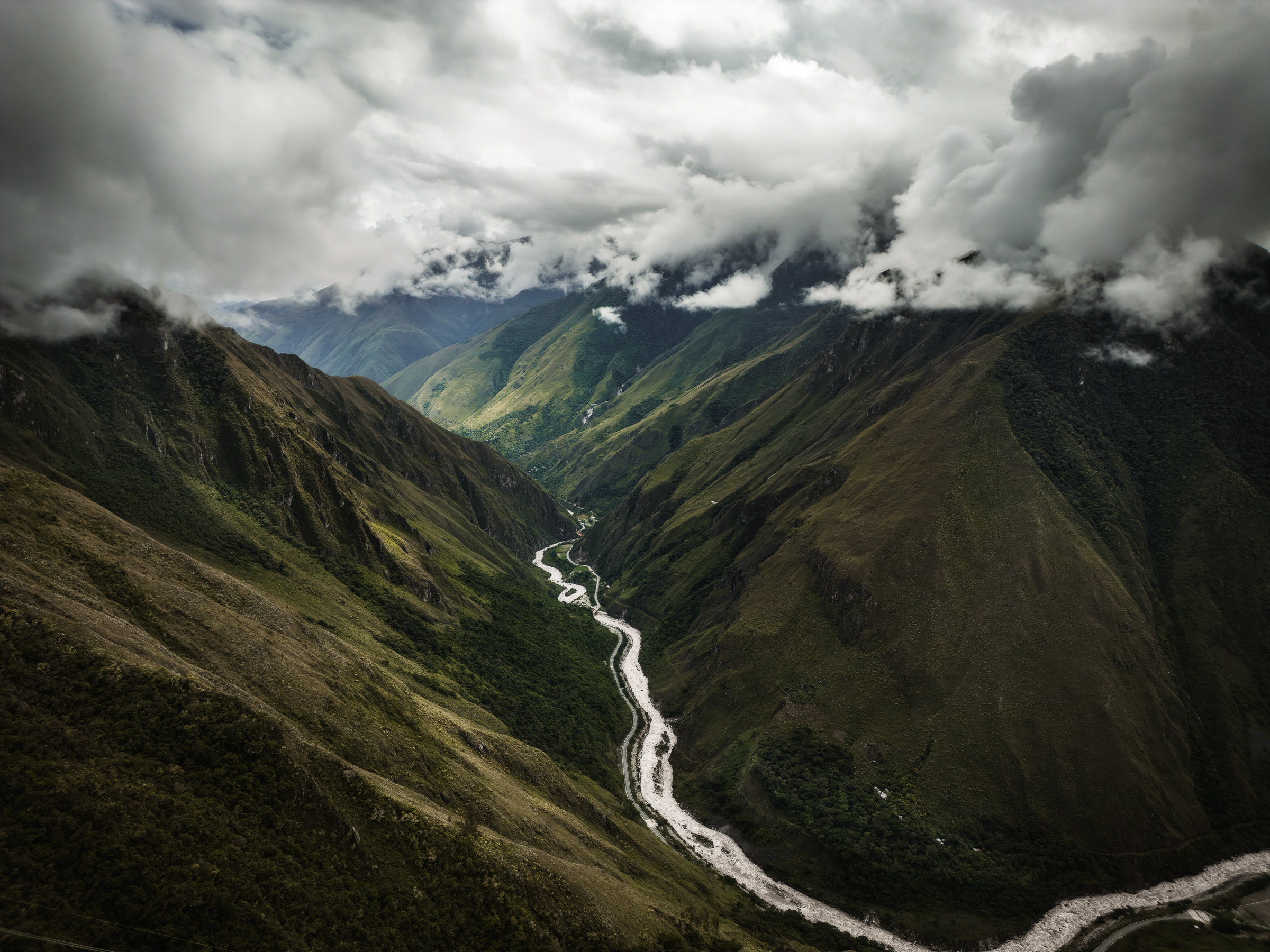 Winding mountain road following a river through a cloud-filled valley
