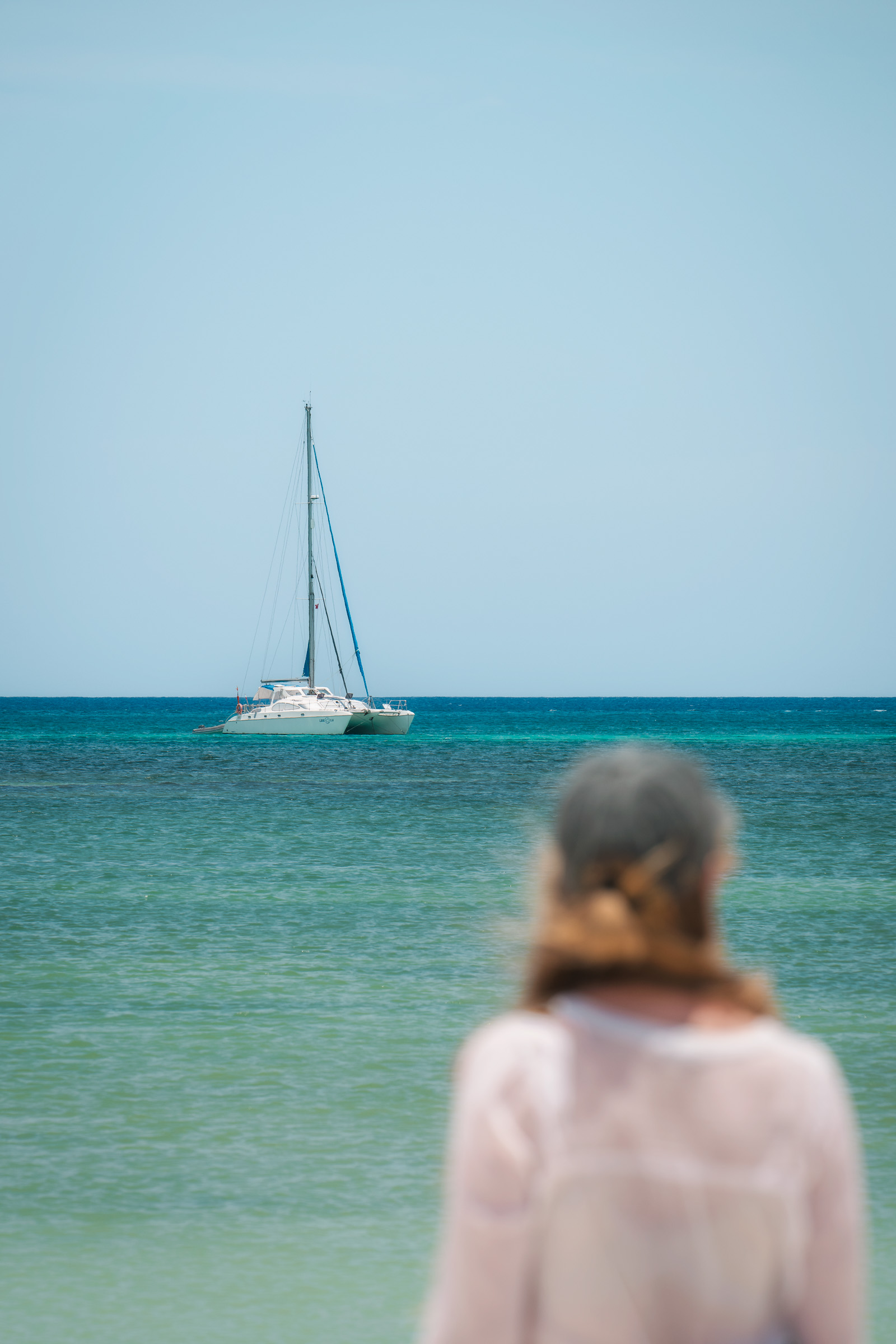 Woman watching a sailboat from the turquoise shore in Aruba