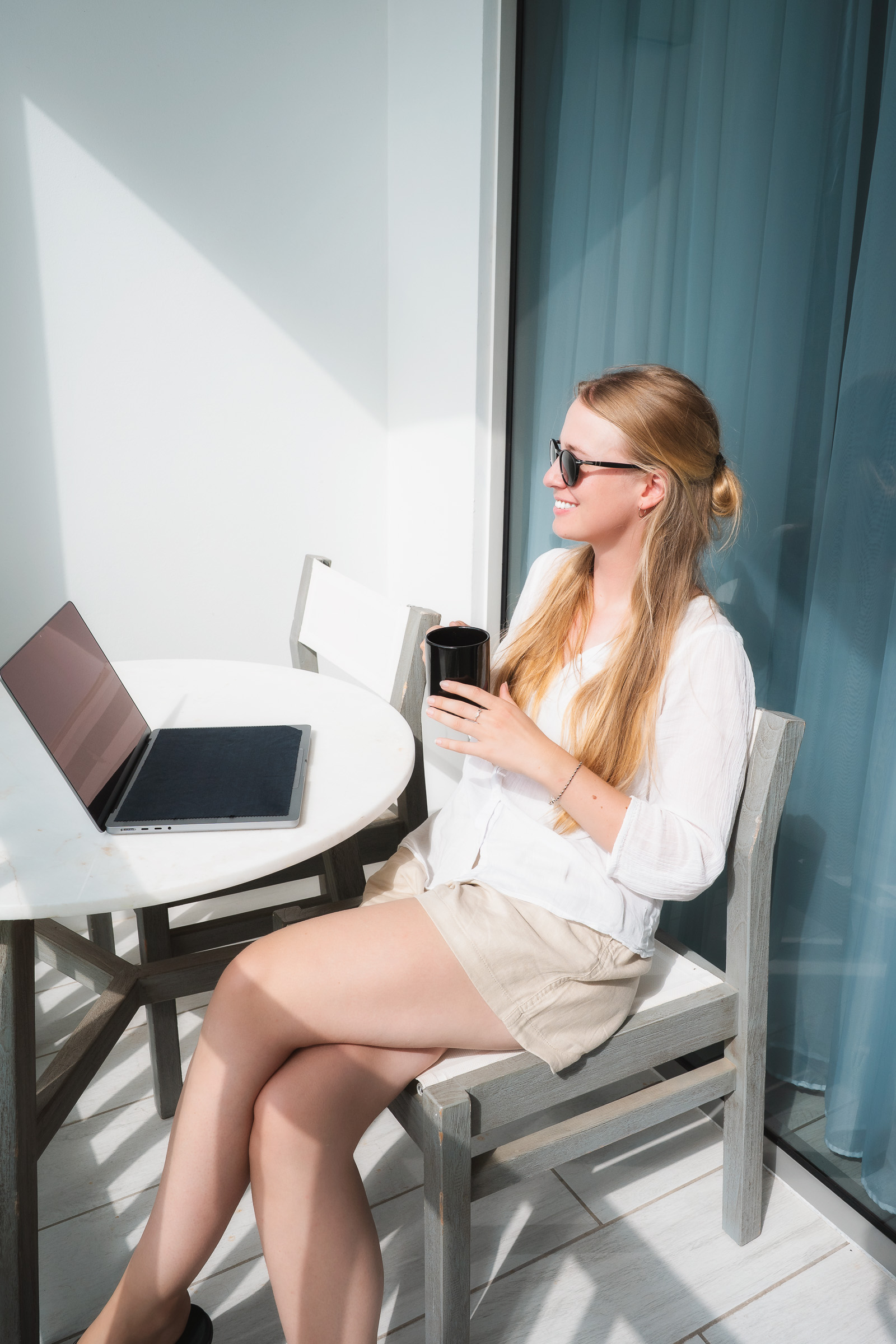 Woman having coffee while working on a laptop on her hotel balcony