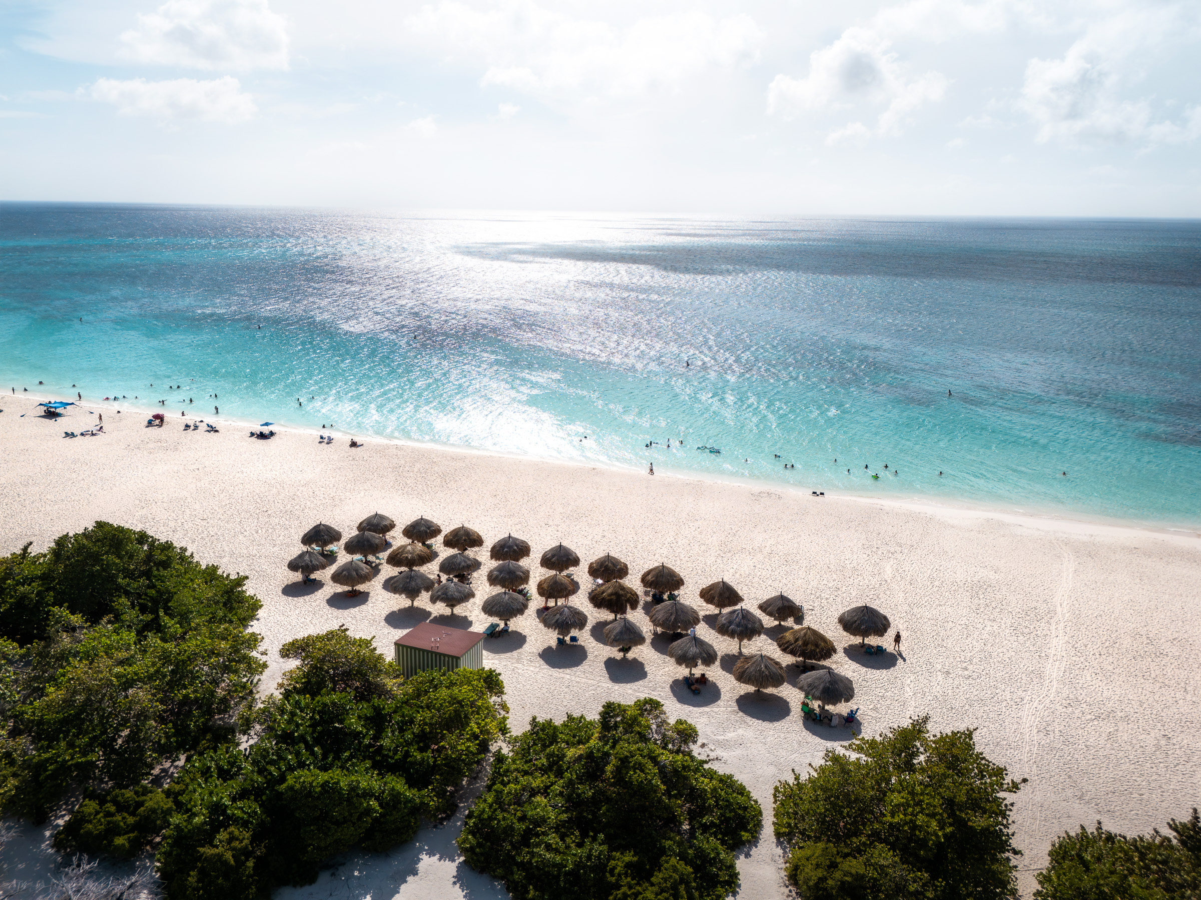Turquoise Caribbean beach lined with rows of thatched sunshades