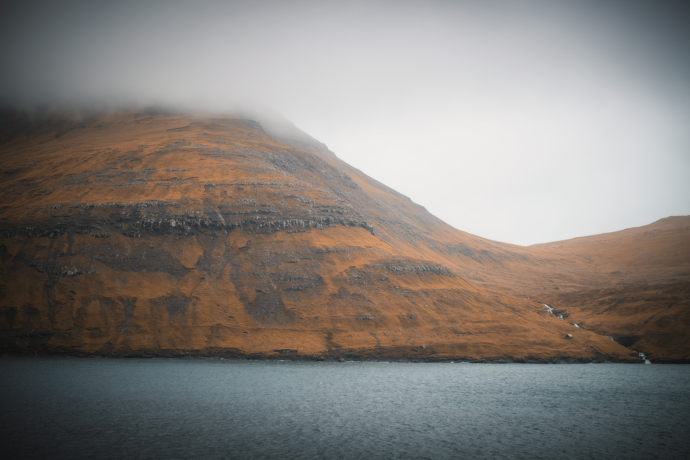 Nebel liegt über einem terrassierten Berg an einem ruhigen Fjord