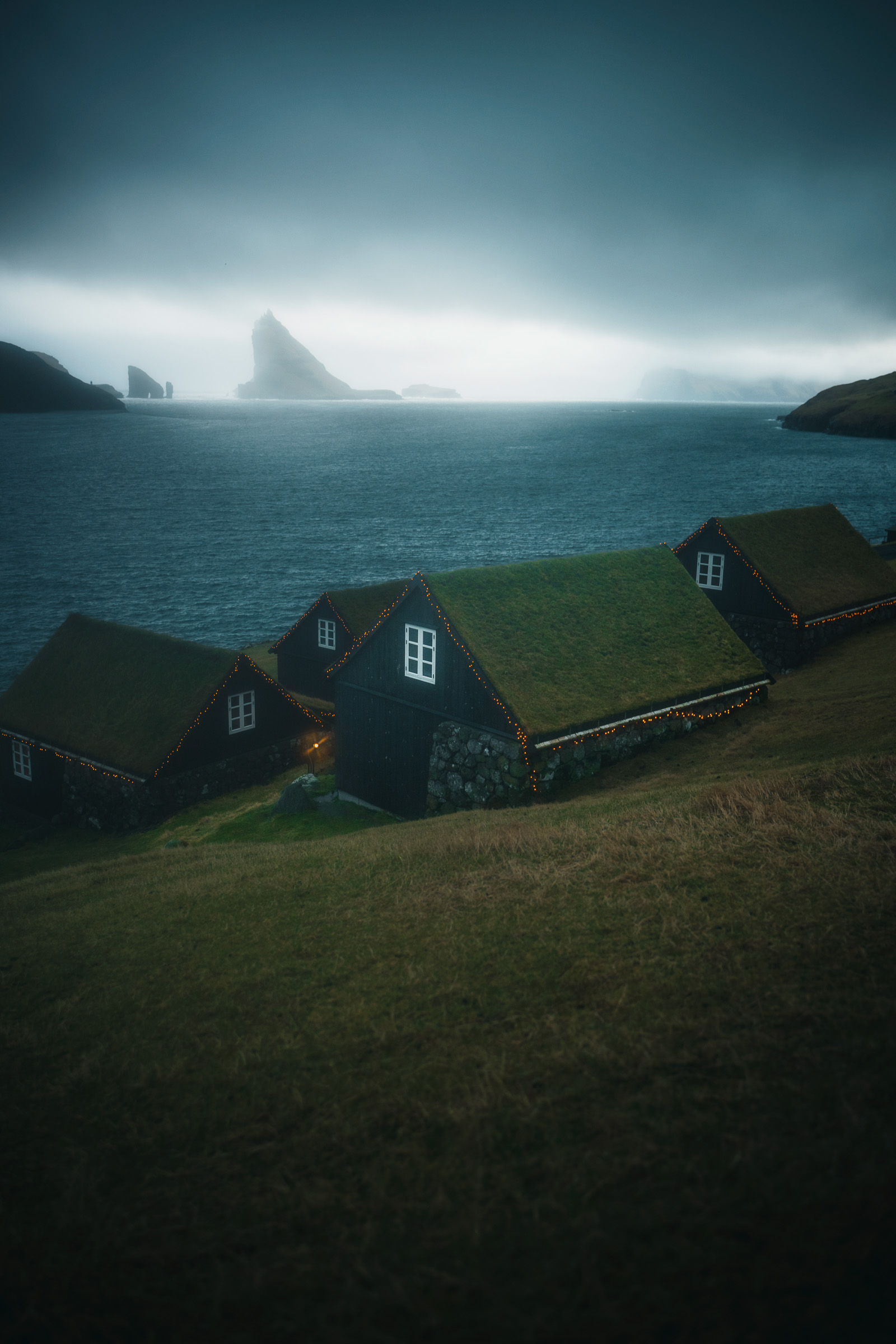 Häuser mit Grasdächern blicken über das Meer auf Tindhólmur