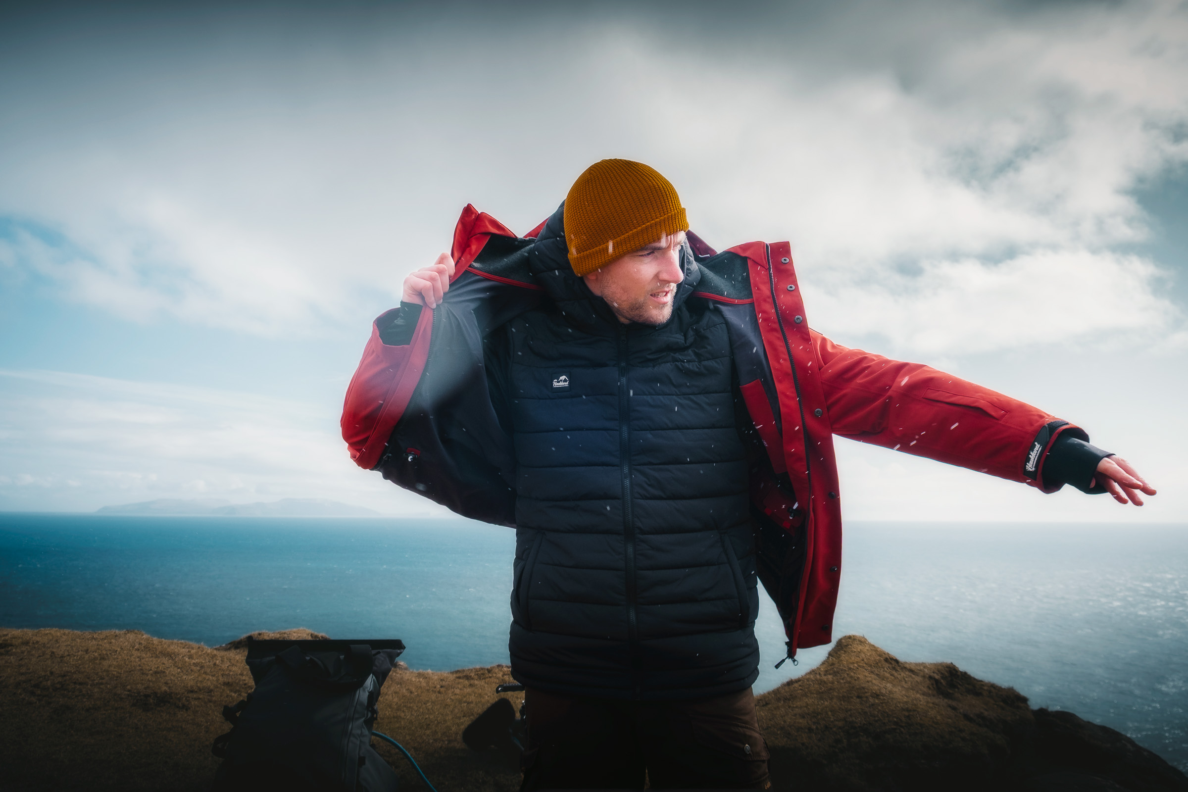 Reisender zieht über dem Meer eine rote Regenjacke an