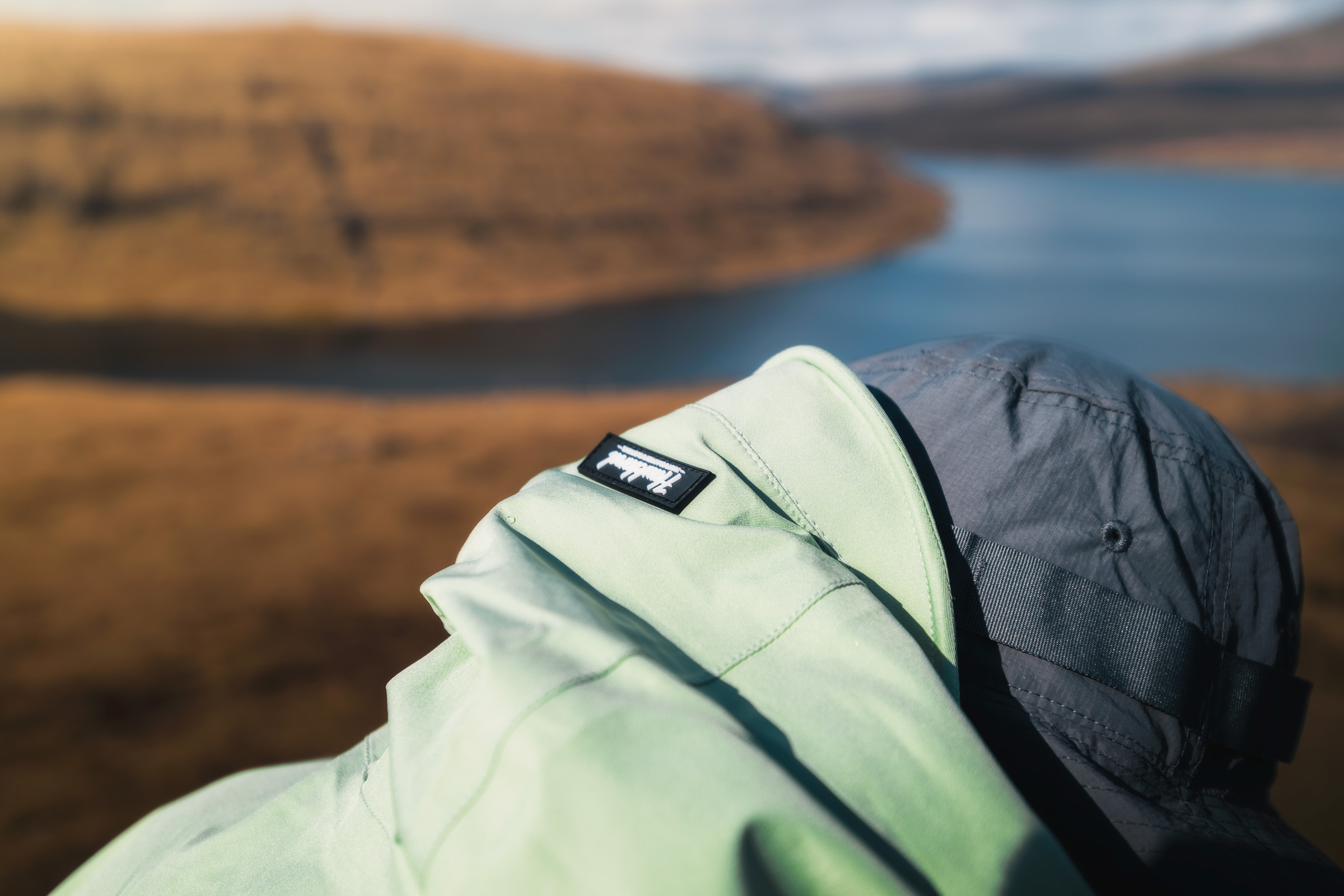 Nahaufnahme einer hellgrünen Kapuze und Kappe über einem Fjord