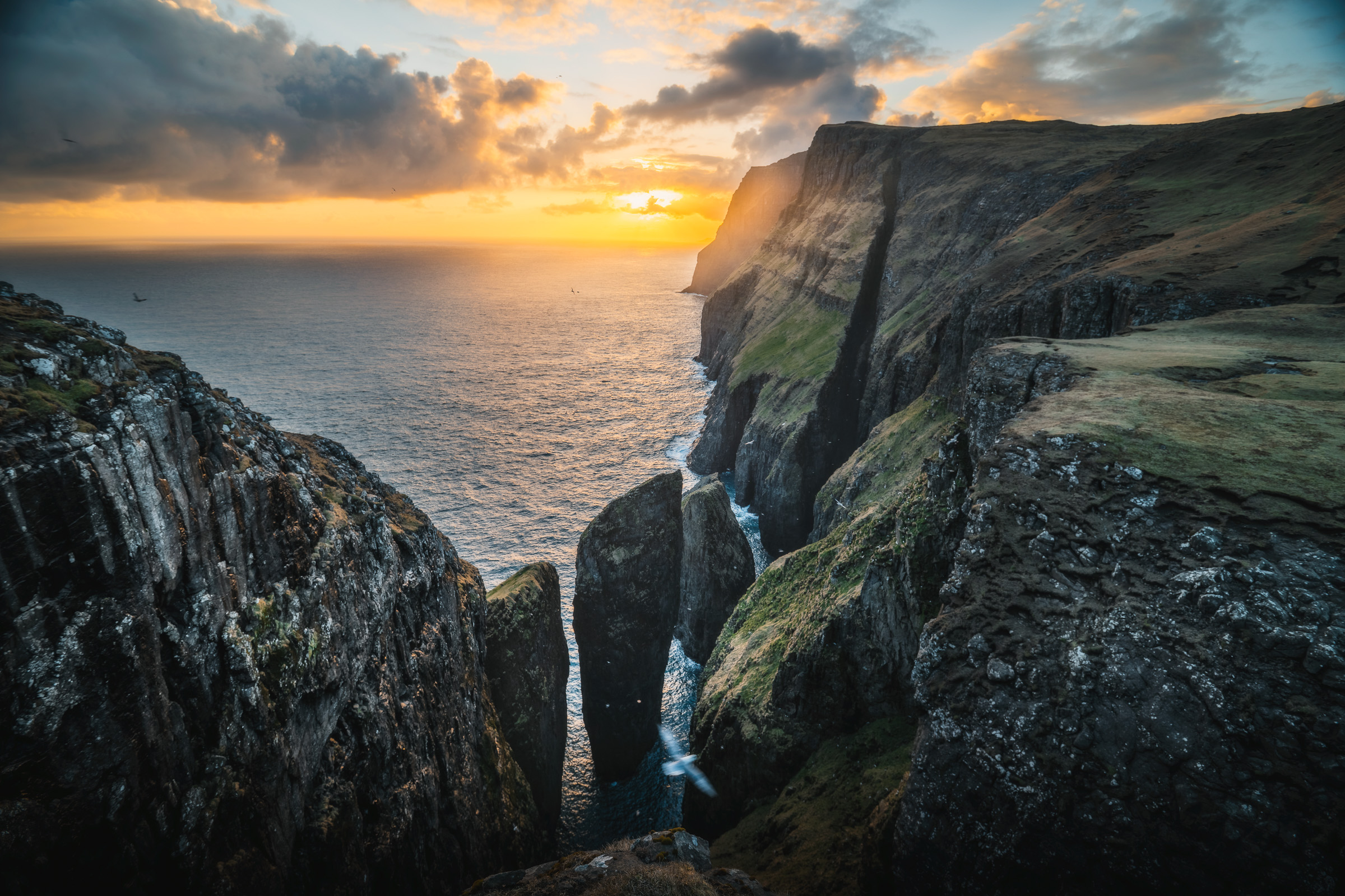 Sonnenuntergang hinter Meeresklippen und einem schmalen Wasserfall