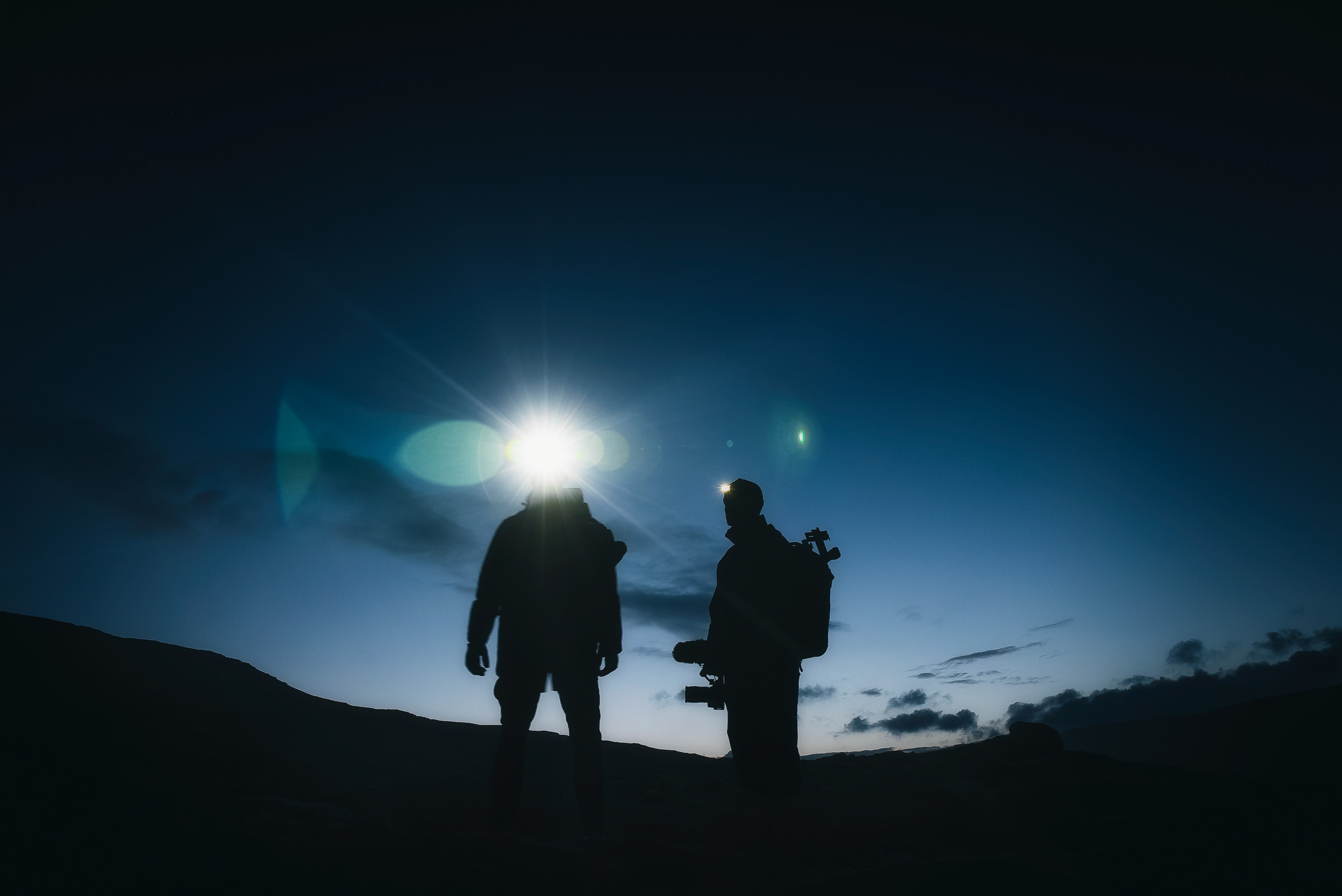 Zwei Reisende als Silhouetten unter einem hellen Mond bei Nacht