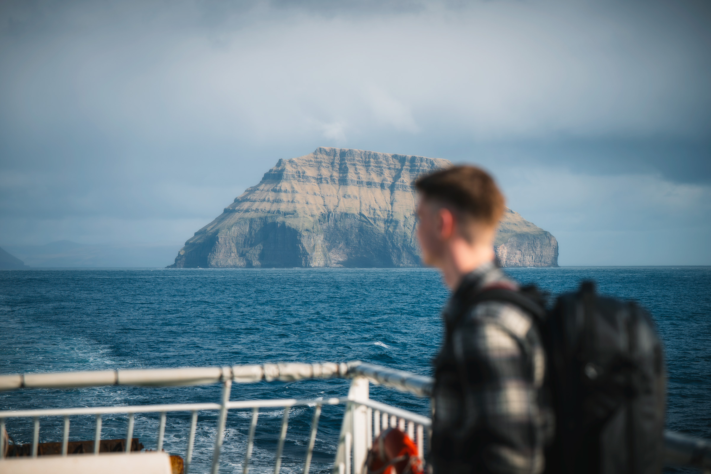 Reisender auf einem Fährdeck vor einer bergigen Insel