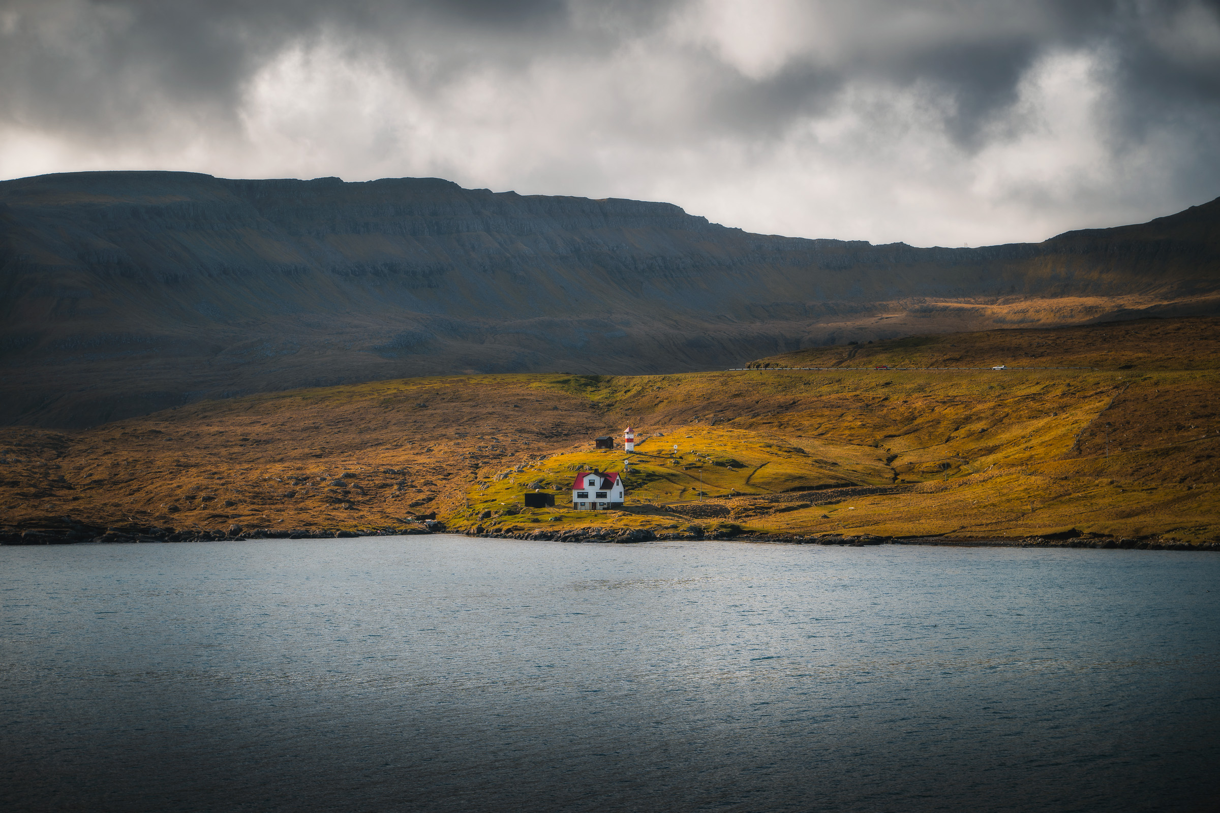 Abgelegene Siedlung am Hang unter dunklen Wolken auf der anderen Seite eines Fjords