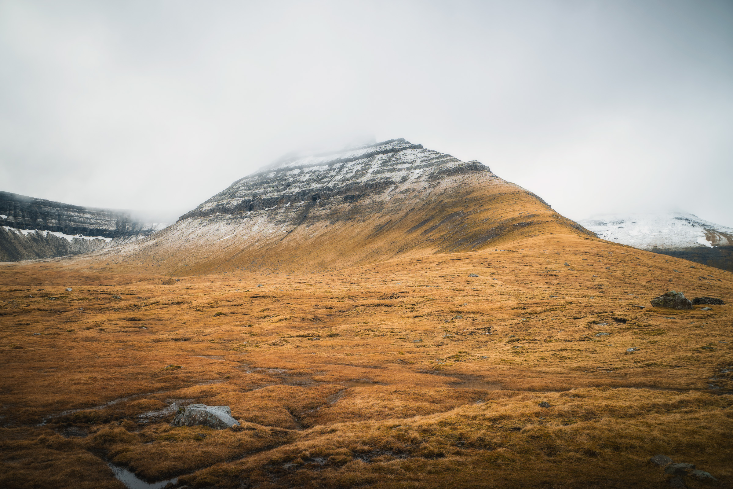 Leicht verschneiter färöischer Berg über goldenem Moorland