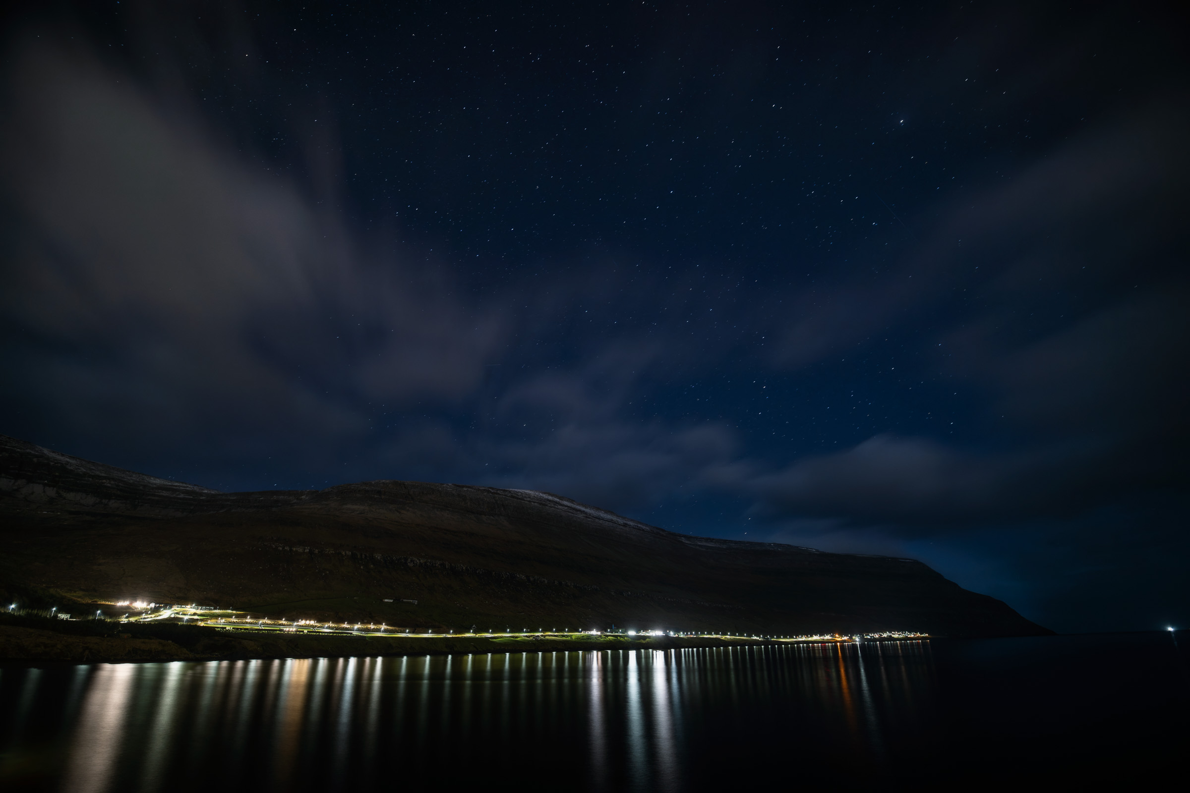 Lichter eines Fjorddorfs spiegeln sich unter einem sternklaren Nachthimmel
