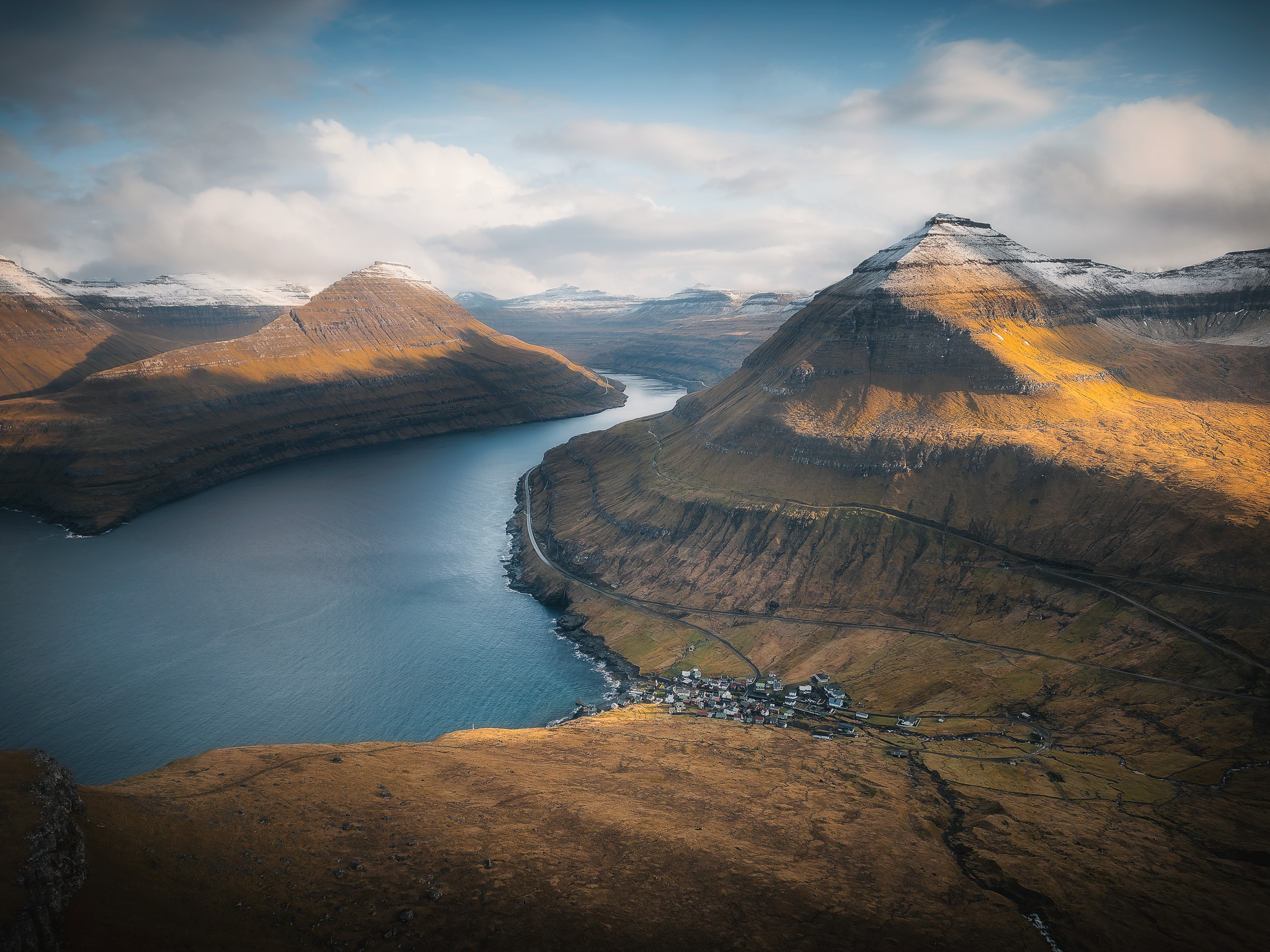 Luftaufnahme eines Fjorddorfs zwischen sonnigen Bergen
