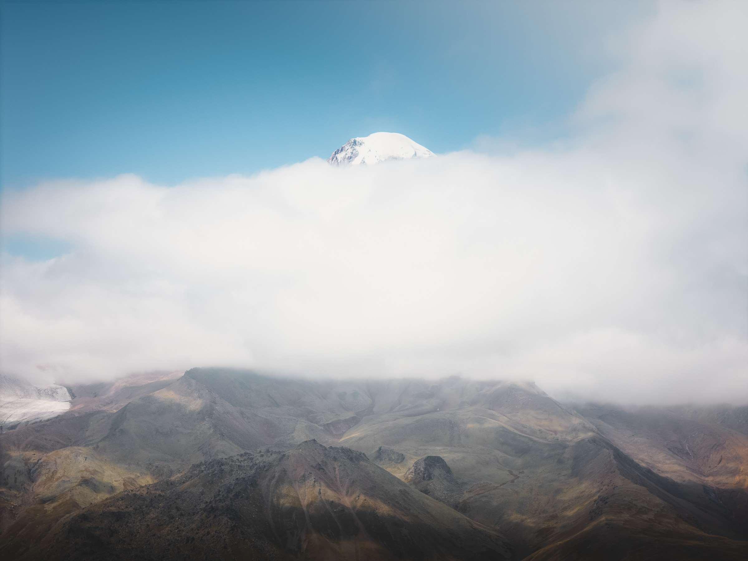 Schneebedeckter Berggipfel ragt über einer geschlossenen Wolkendecke auf