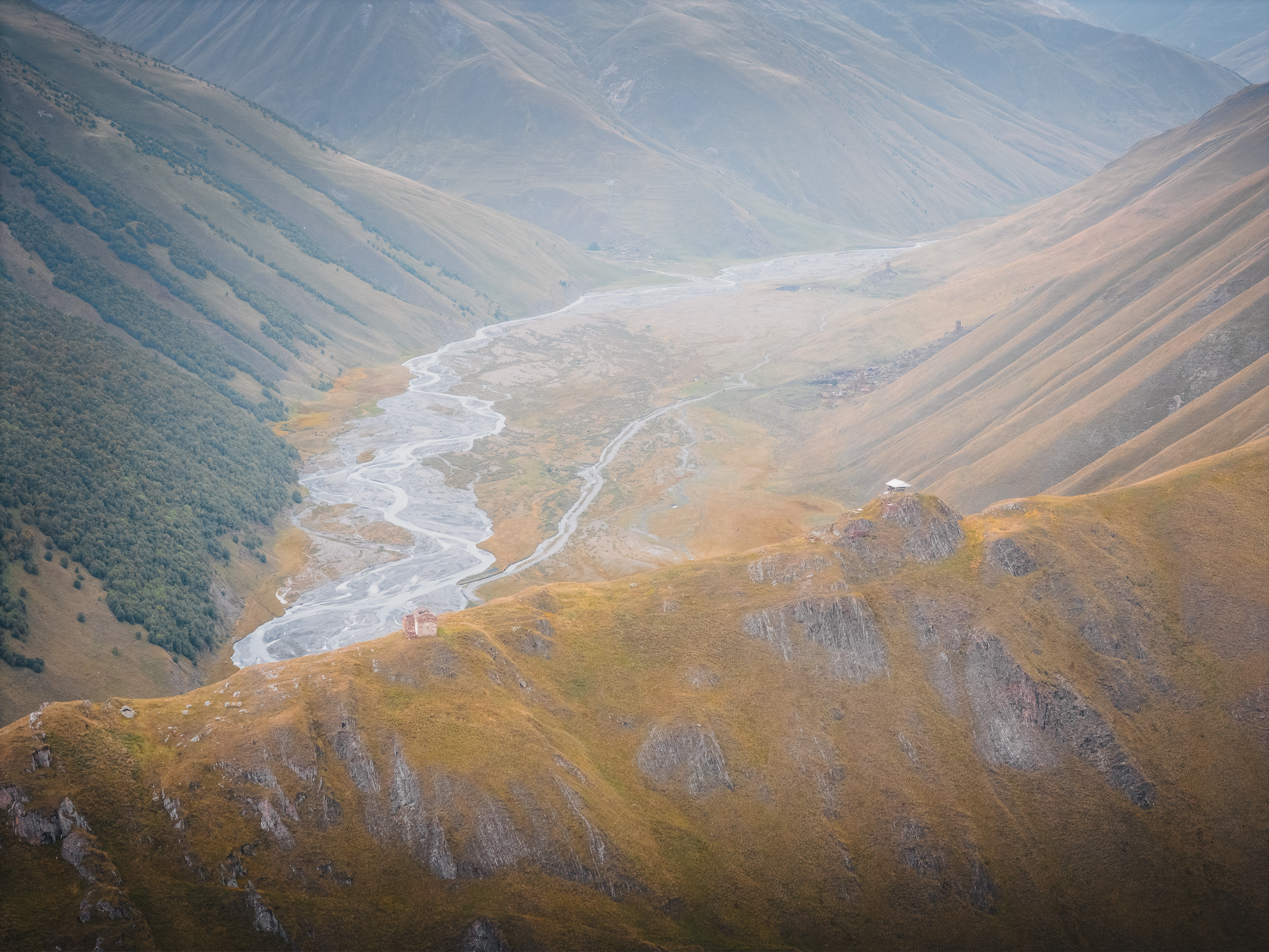Gewundener Fluss durch ein weites herbstliches Gebirgstal
