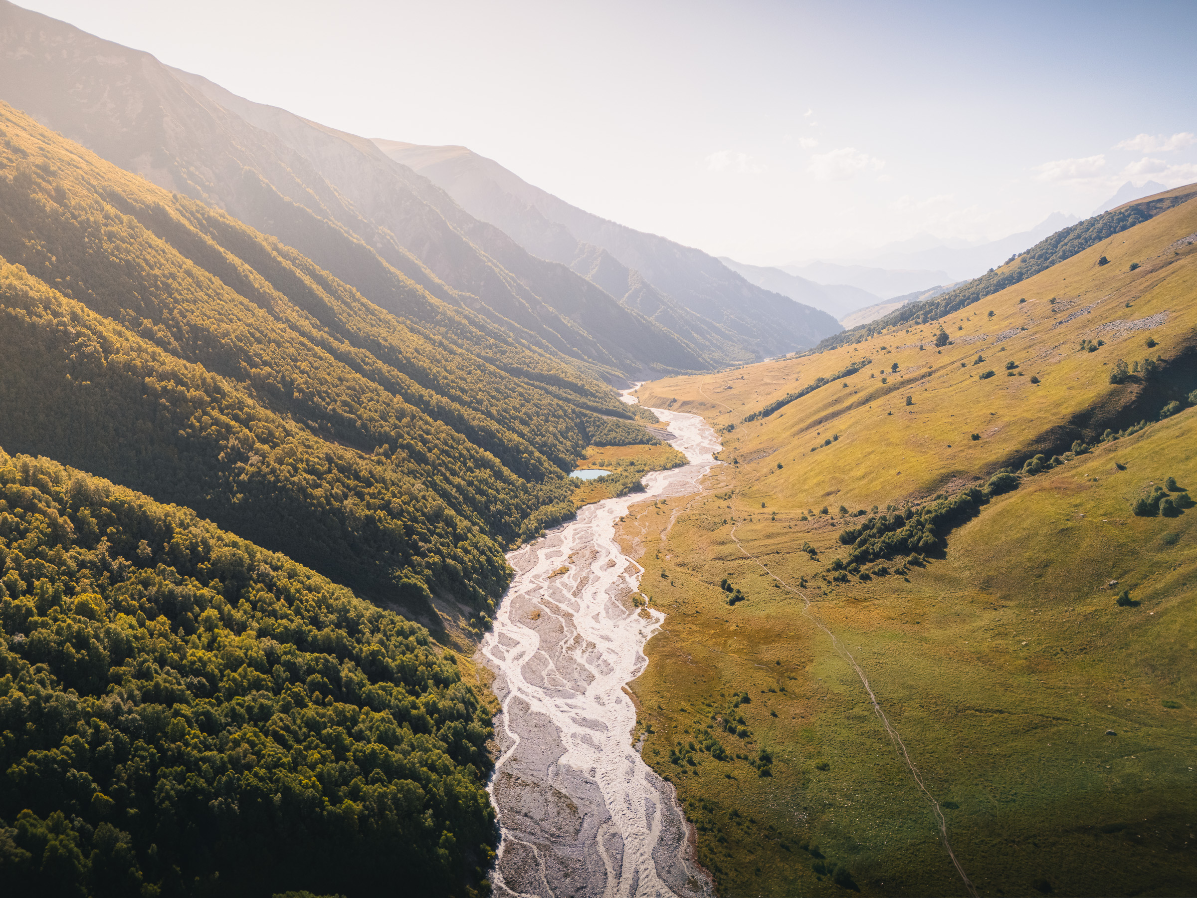 Verzweigter Gebirgsfluss schlängelt sich durch ein sonniges Tal im Kaukasus