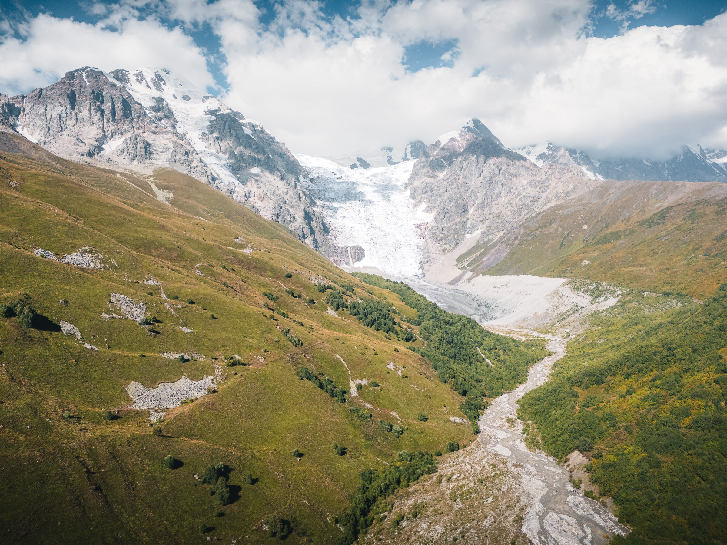 Gletscher zwischen schneebedeckten Gipfeln über einem grünen Tal