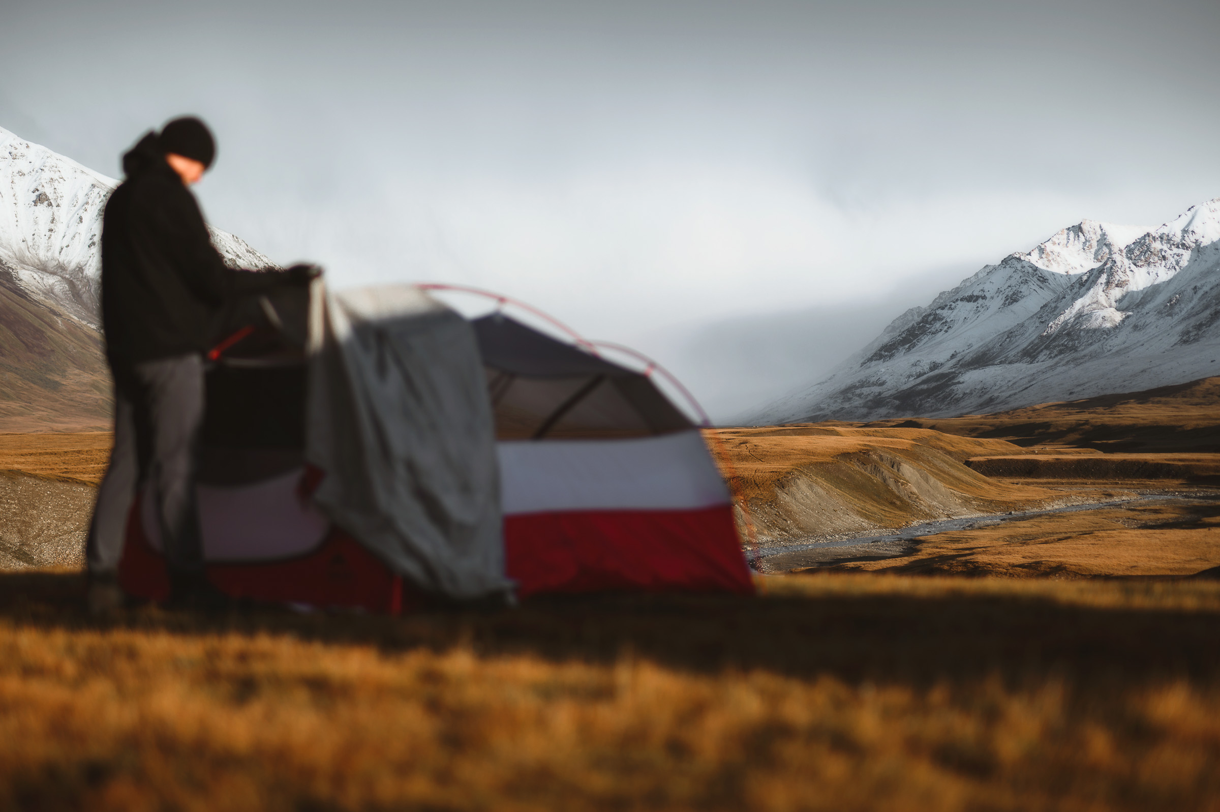 Traveler standing beside a tent beneath snowy mountains