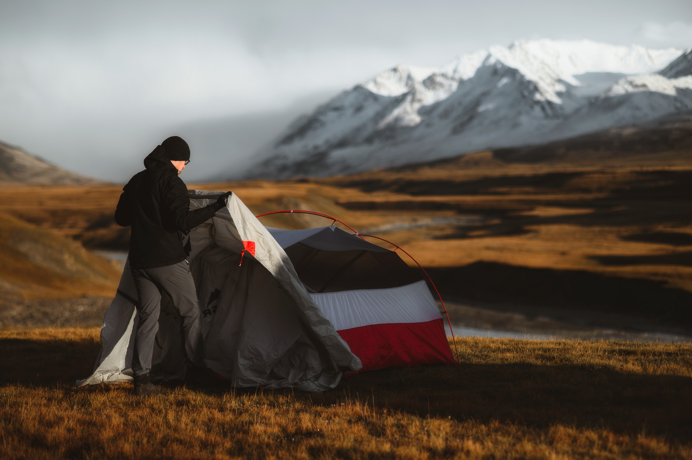 Traveler pitching a tent with a snow-covered range beyond