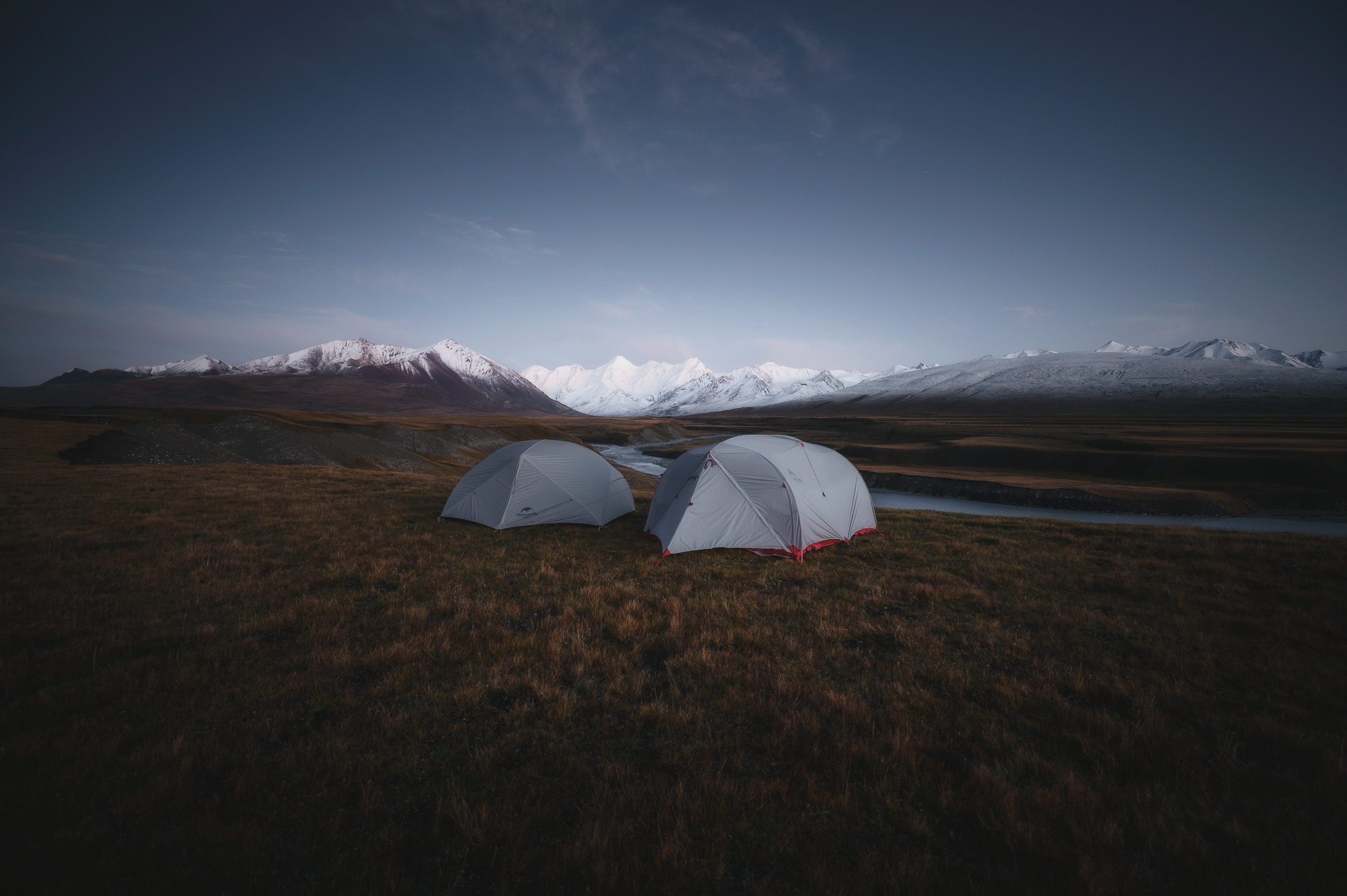Two tents at blue hour beneath a snow-covered range