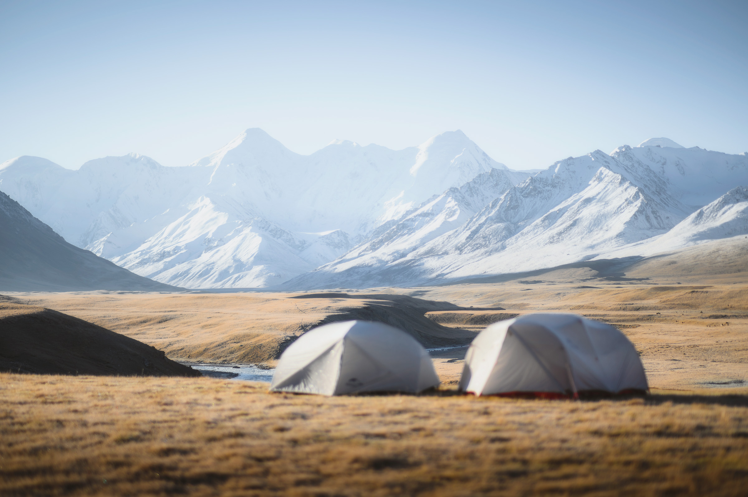 Two tents beneath a vast snow-covered mountain range