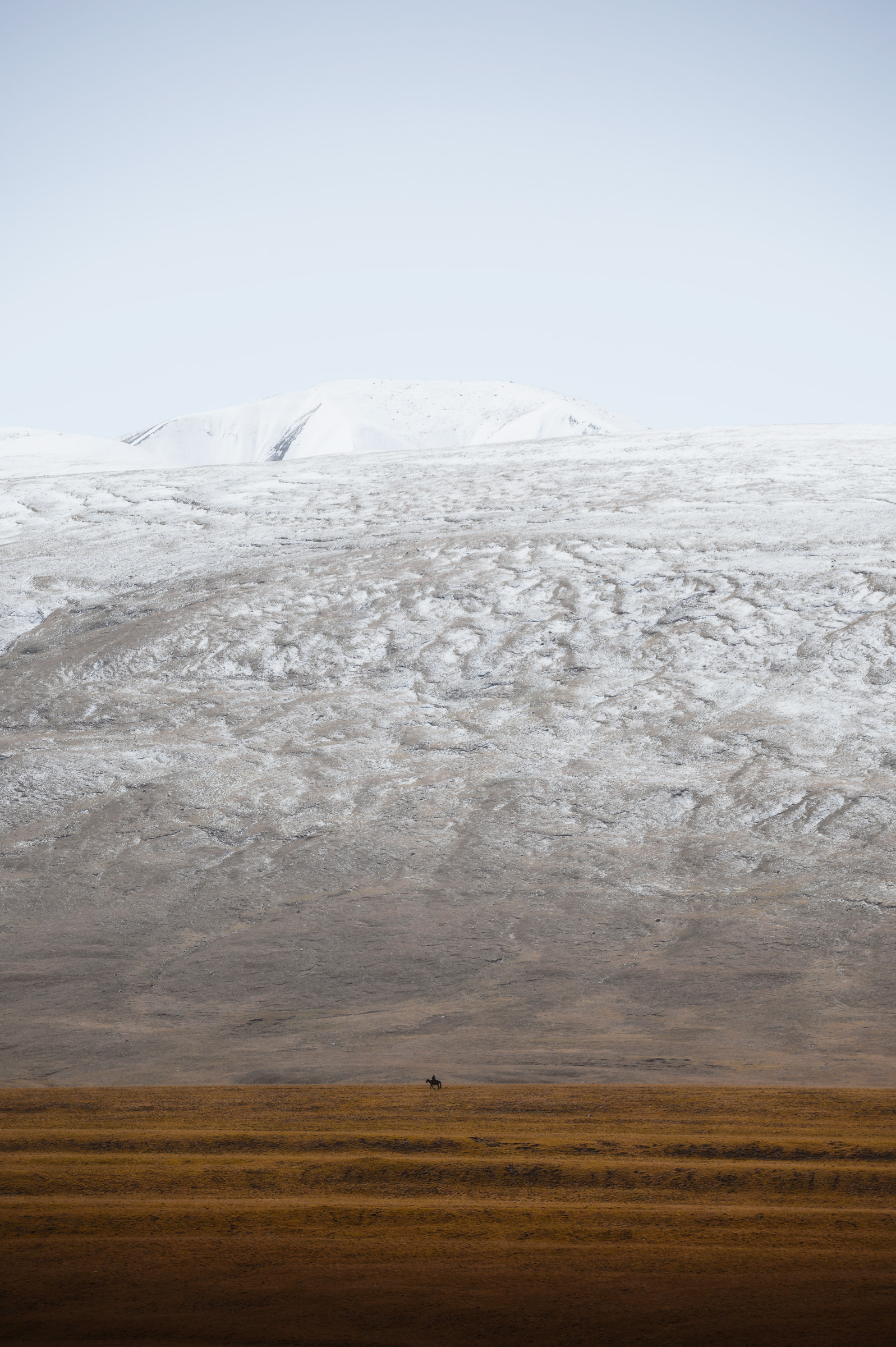 Lone hiker crossing a plain beneath an immense snowfield
